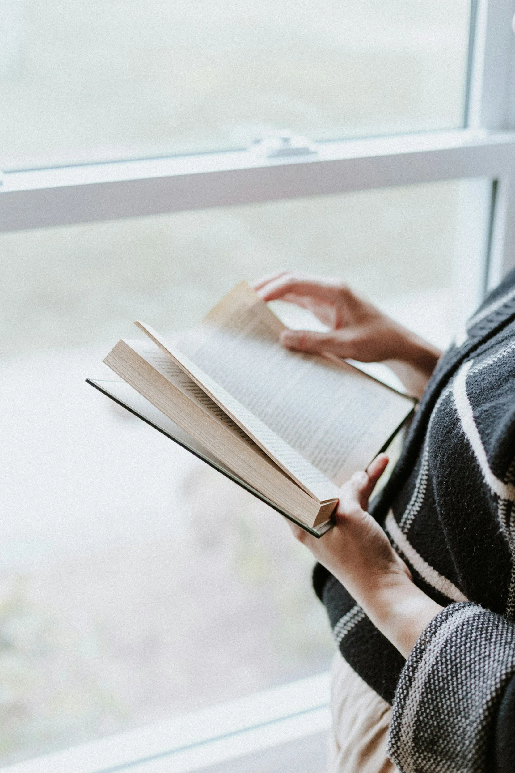 A woman holding a book looking out a window representing using coping skills after a eating disorder therapy session in Salt Lake City.