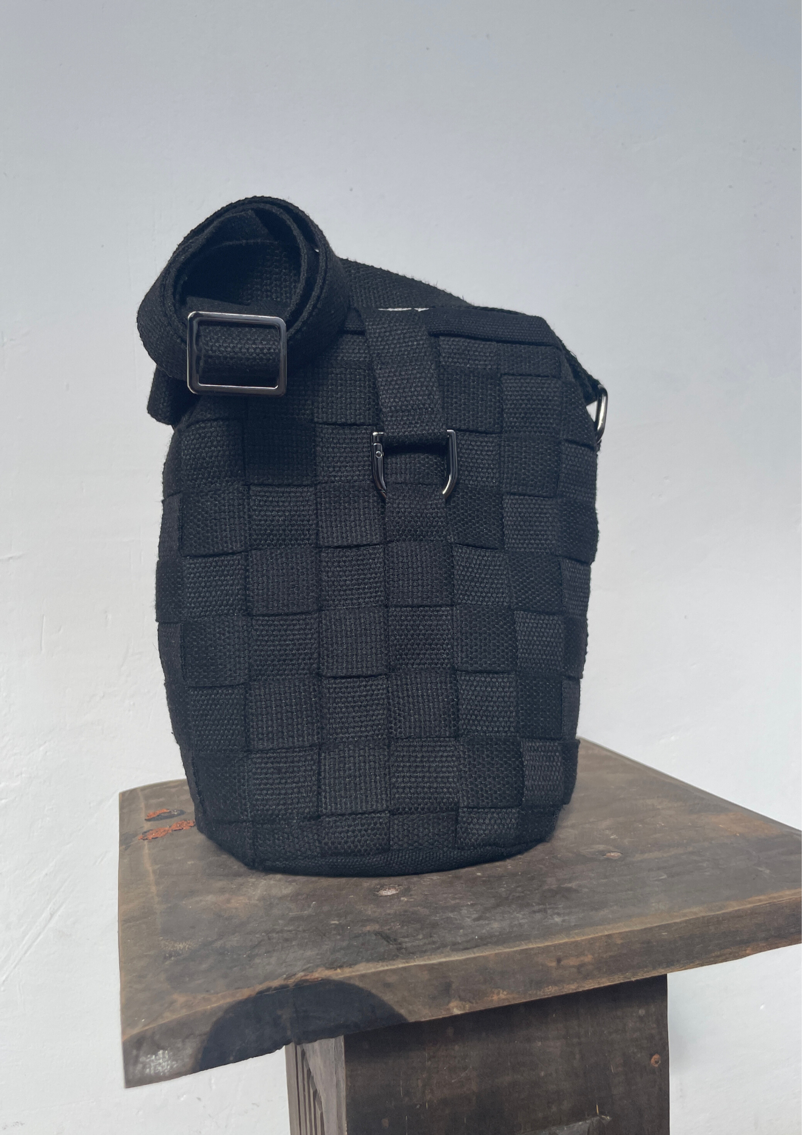 Black tactical elastic strap bag or pouch sitting on a wooden surface against a plain white wall.