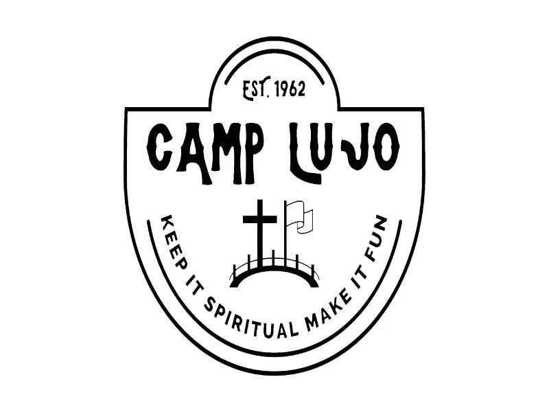 Black and white logo for Camp Lujo with a shield shape, Christian cross, a flag, and a curved fence, with the slogan 'Keep it spiritual Make it fun'.
