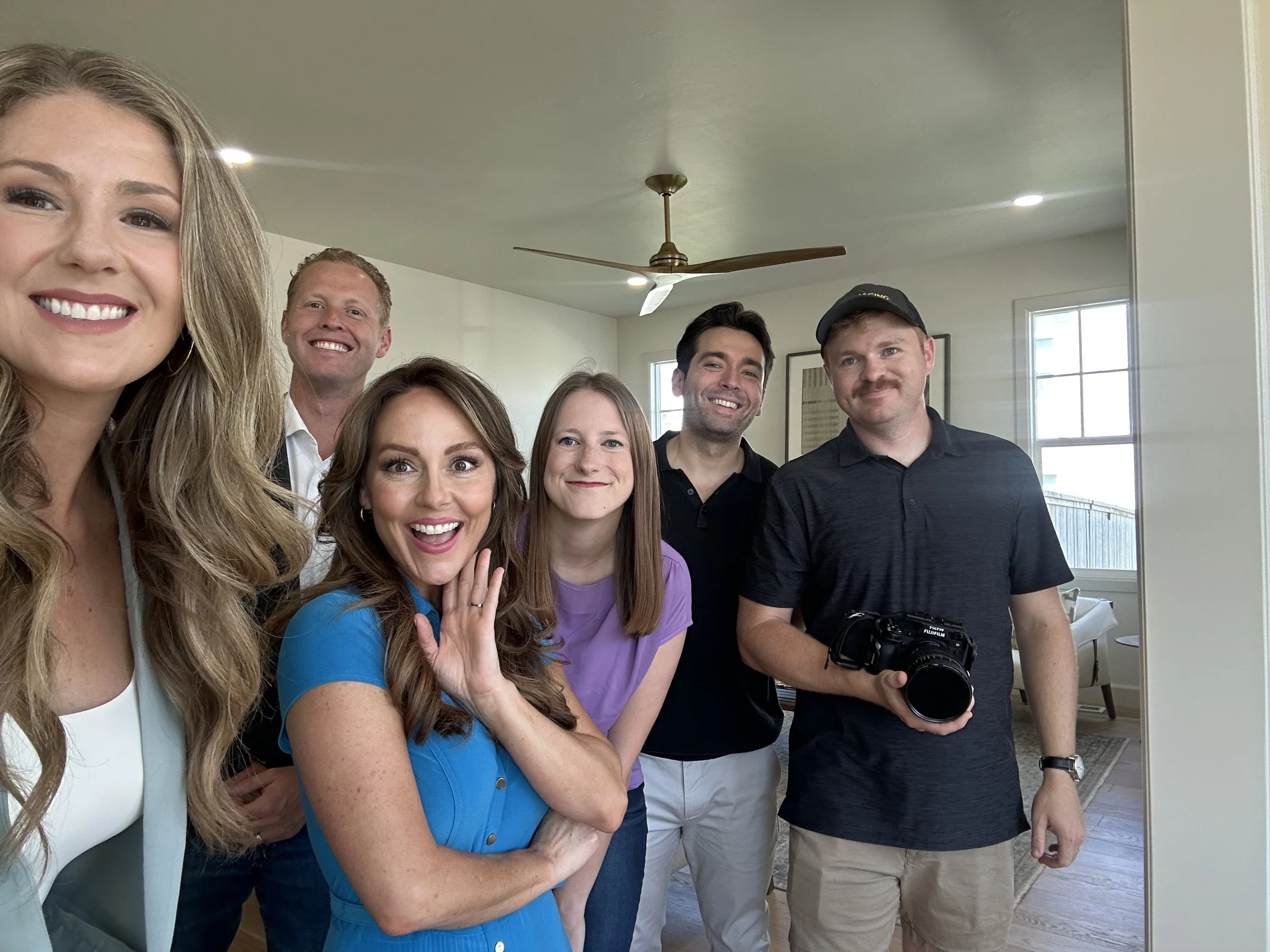 Group of six people taking a selfie inside a living room, smiling and posing.