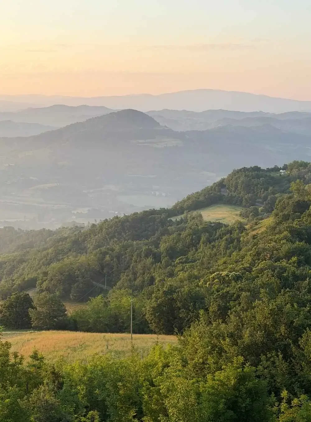 A scenic view of rolling green hills and mountains, with layers of distant peaks fading into the sky during sunset or sunrise.