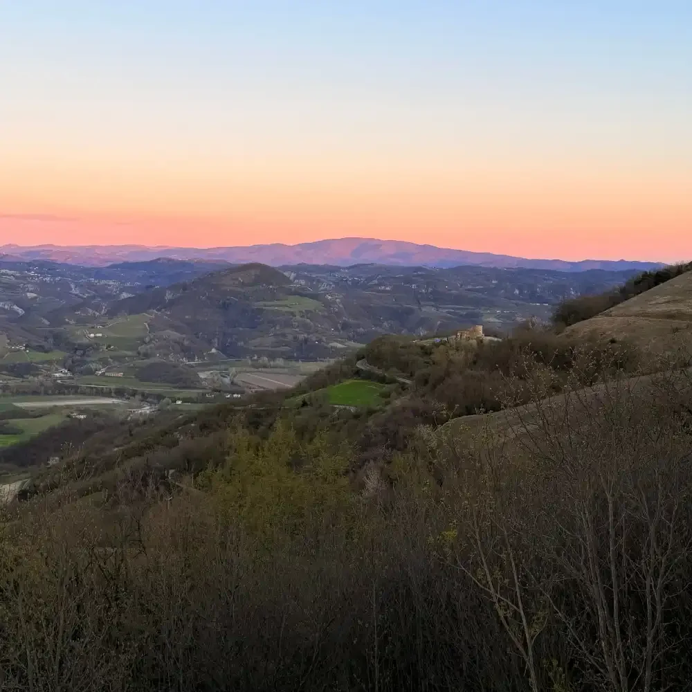 Scenic view of rolling hills and mountains at sunset with a colorful sky in the background.