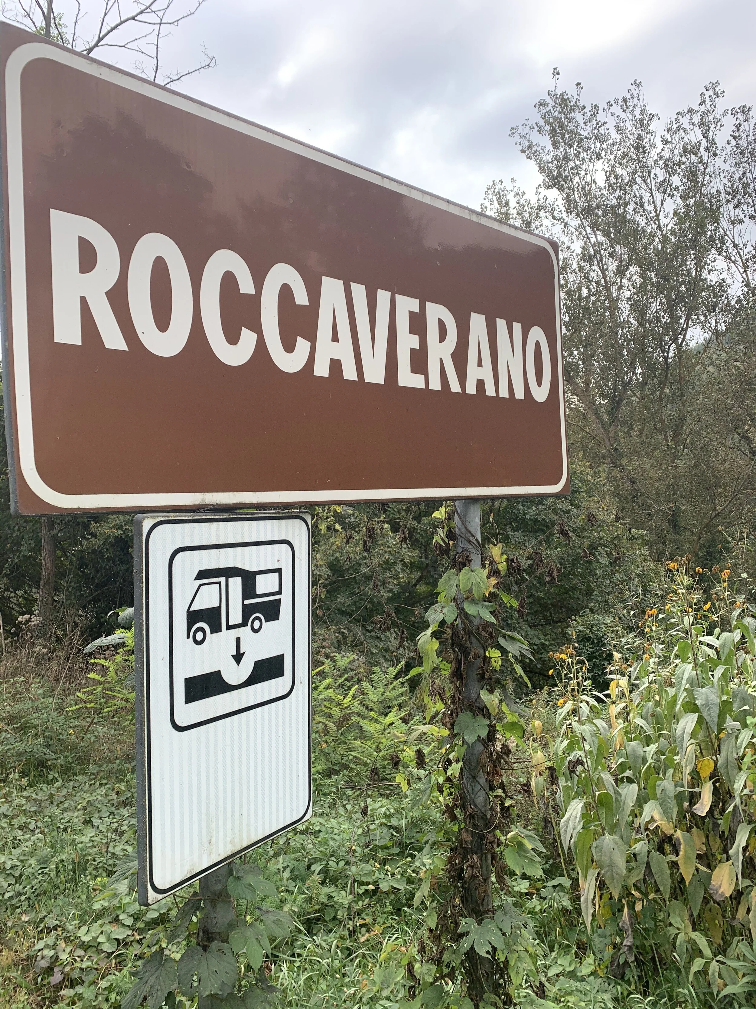 Brown sign that reads 'ROCCAVERANO' and a smaller white sign below with a bus icon and downward arrow.