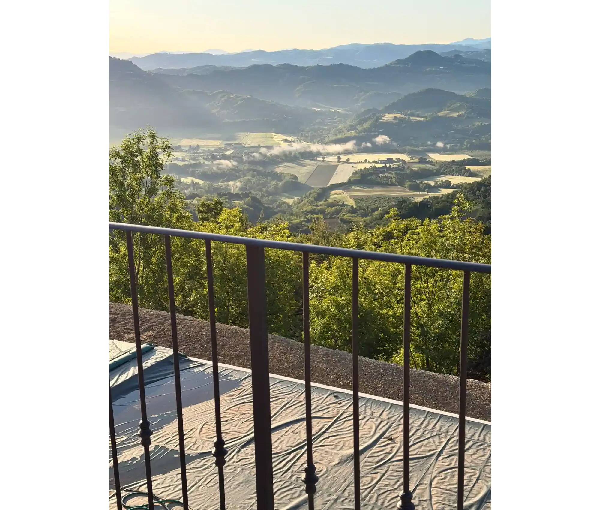 View of rolling hills and mountains in the distance with a valley below, seen from a balcony with a metal railing and a beige blanket or cover on the ground.