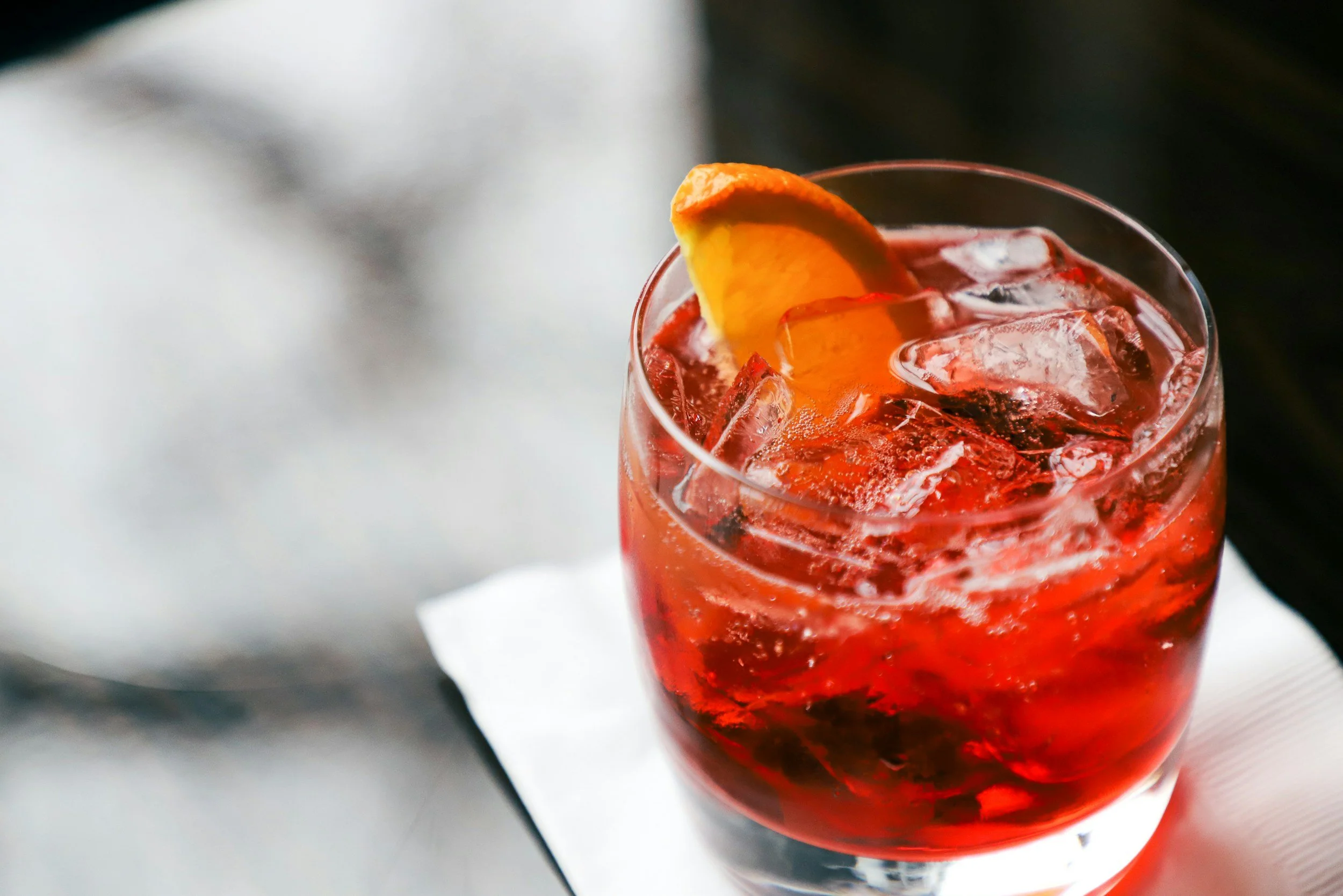 A glass of red drink with ice and a lemon wedge garnish.