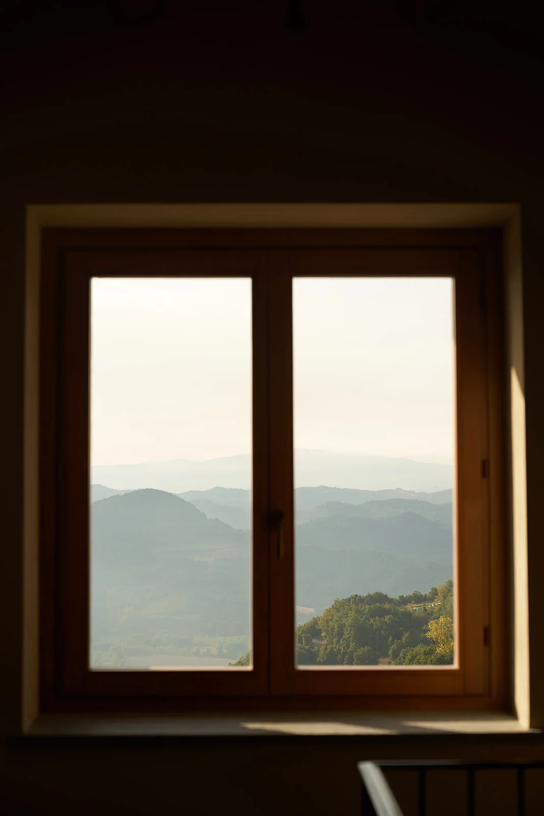 View through a window showing distant mountain ranges and hills with trees.