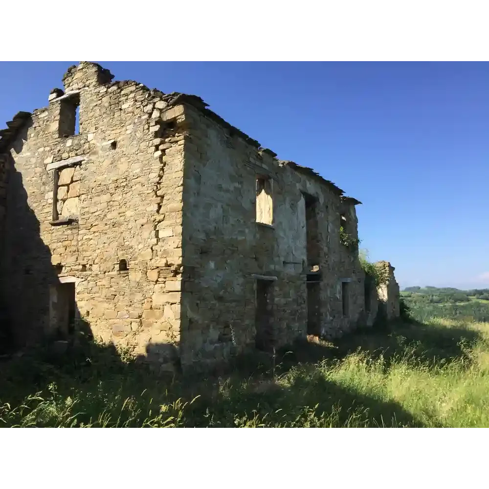 Dilapidated stone building in a grassy field with a clear blue sky.