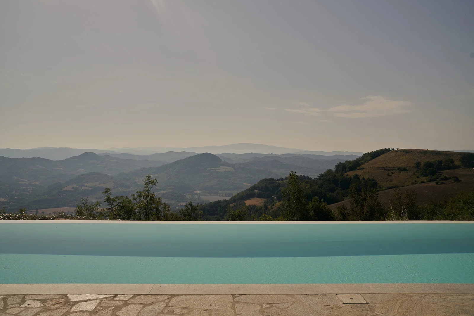 Pool with mountain landscape and hills in the background under a cloudy sky.