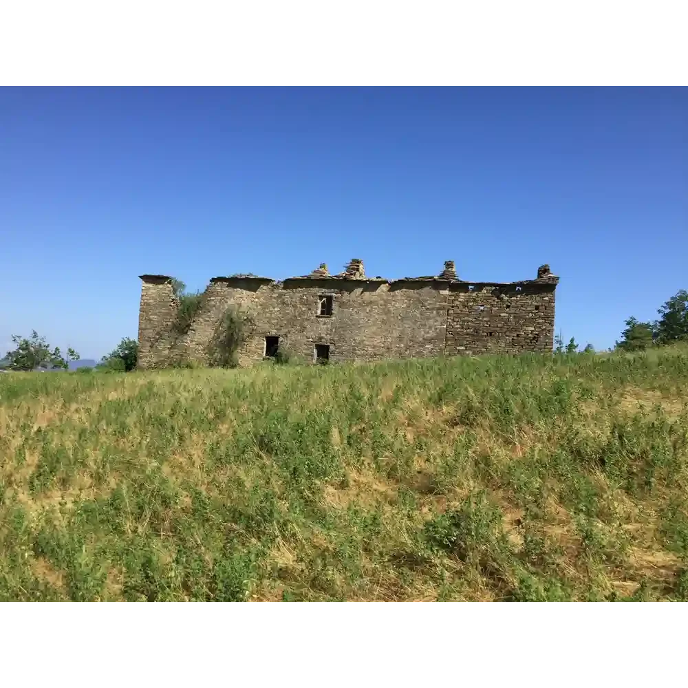 Ruined stone building on a grassy hill under clear blue sky.