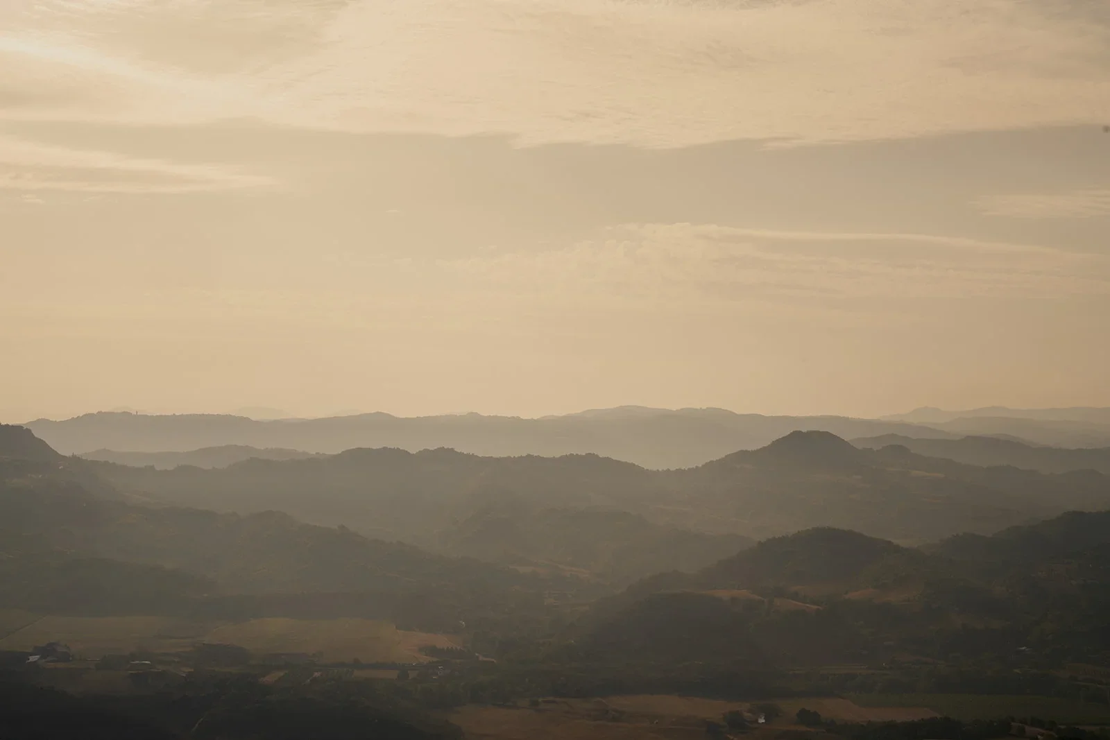 Hazy landscape of rolling hills and mountains with a cloudy sky.