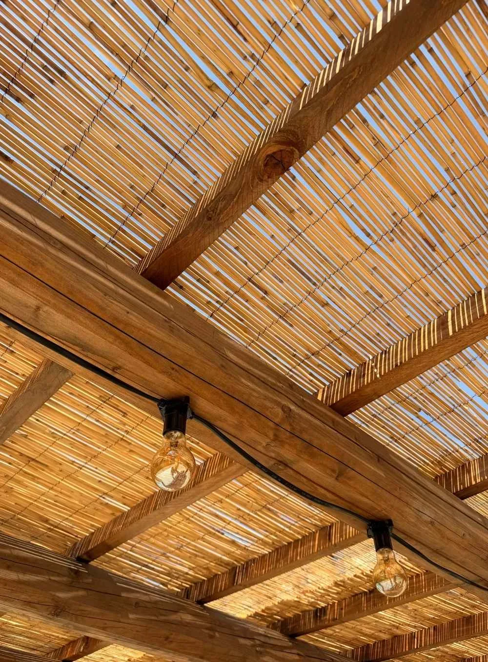 Close-up view of a wooden and bamboo pergola roof with two hanging light bulbs.