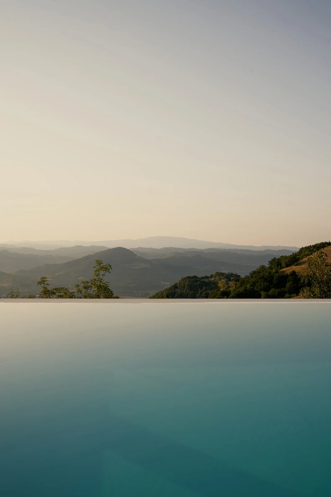 Scenic view of rolling hills and mountains in the distance during sunset, with a reflective body of water in the foreground.