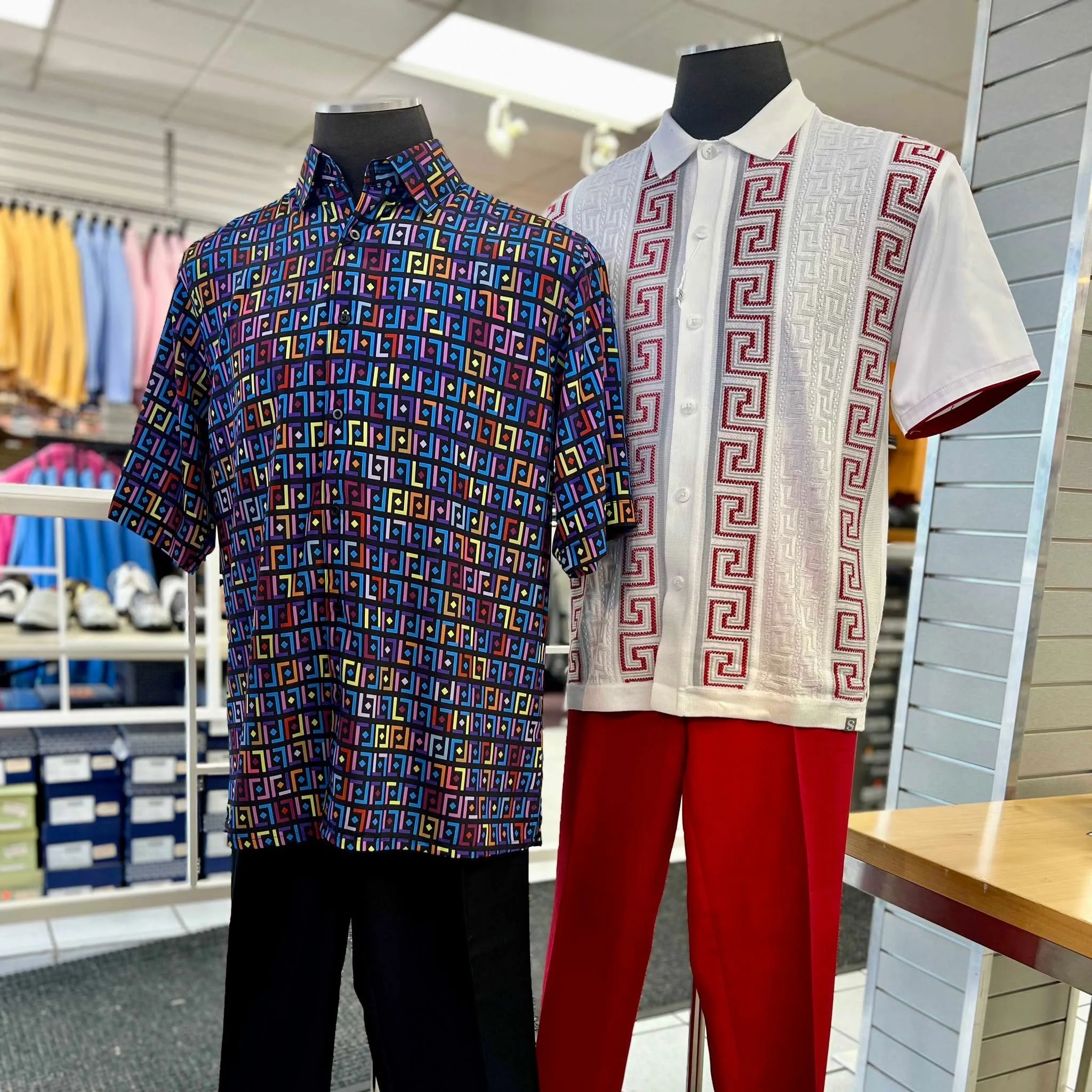 Two mannequins modeling colorful geometric-patterned shirts and pants in a clothing store.
