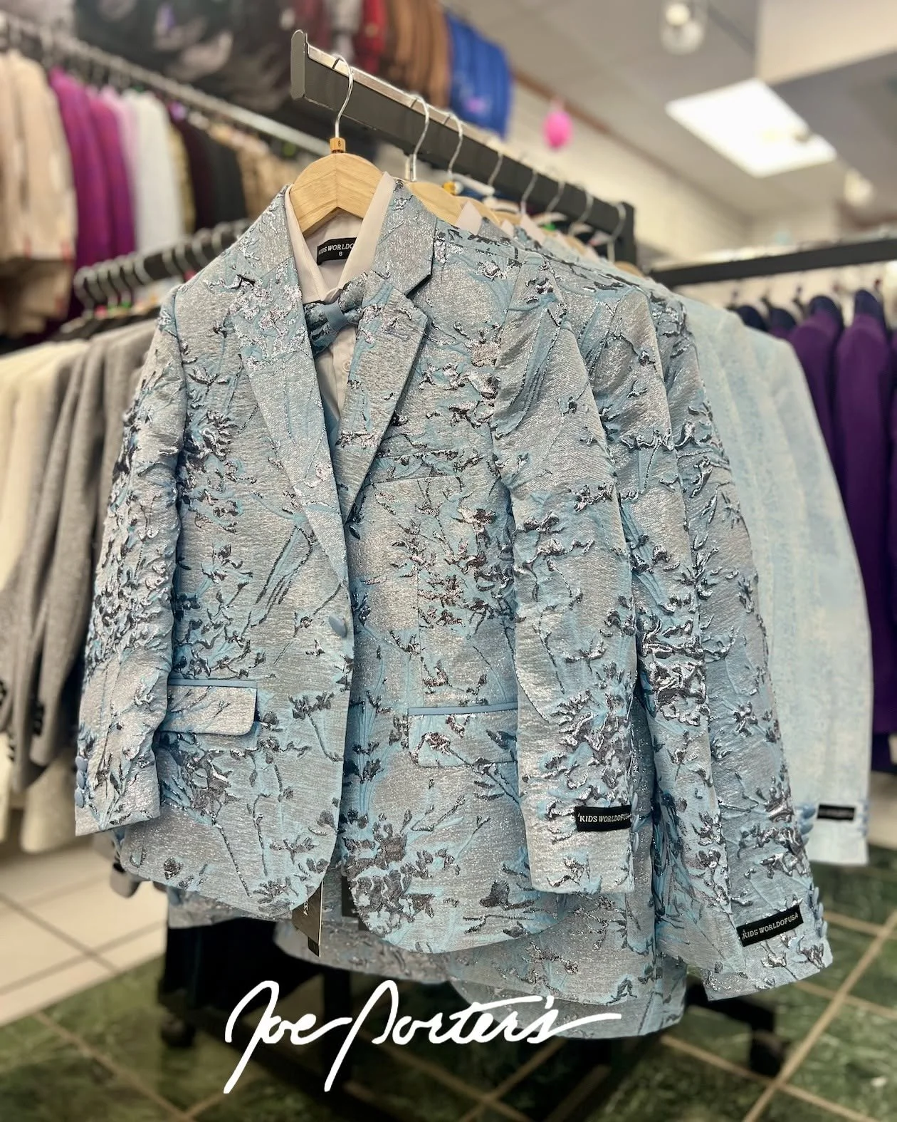 Light blue patterned kids' blazer displayed on a wooden hanger in a clothing store
