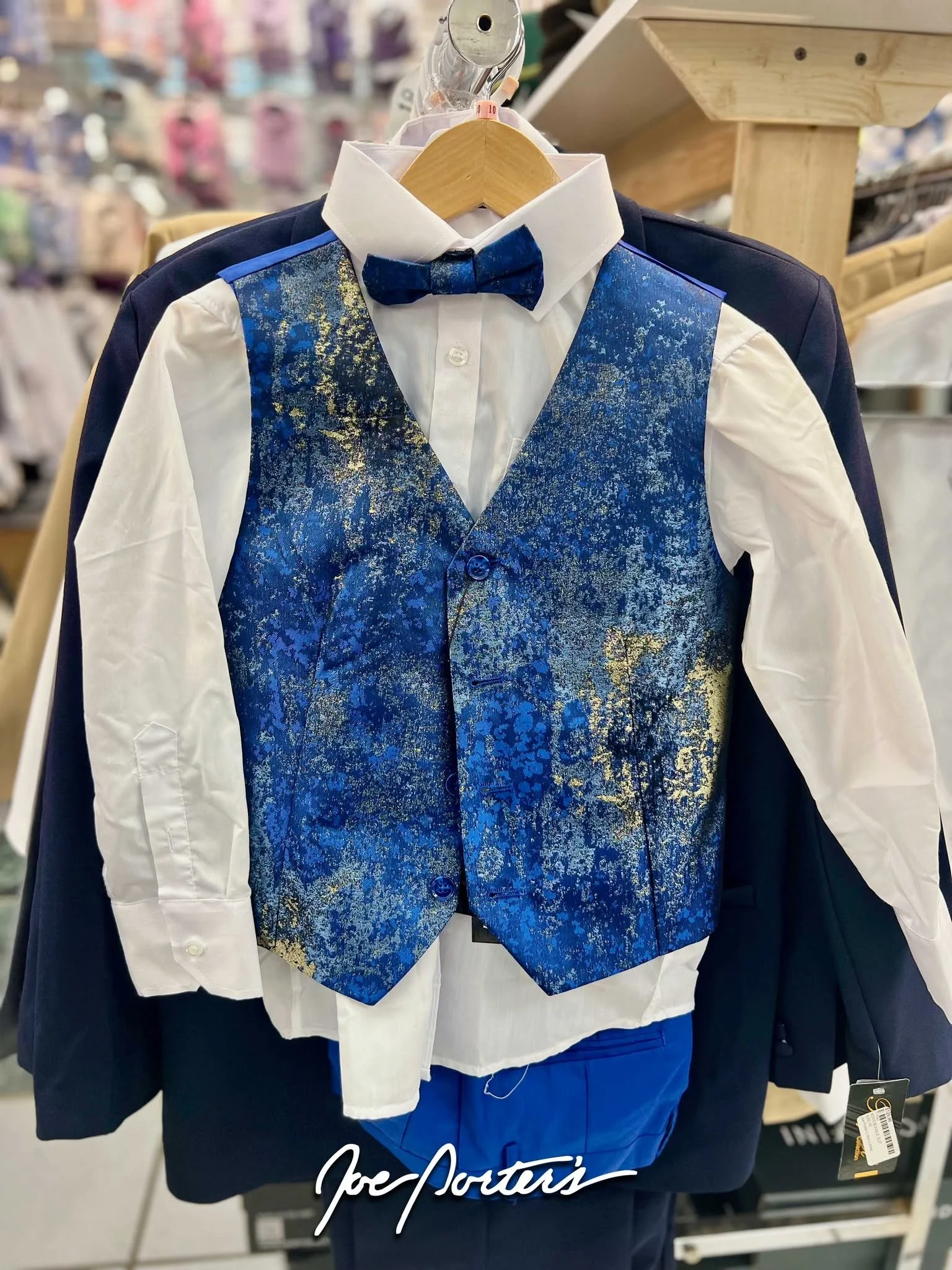 Children's blue patterned vest suit with white dress shirt, navy jacket, and bow tie on a retail display