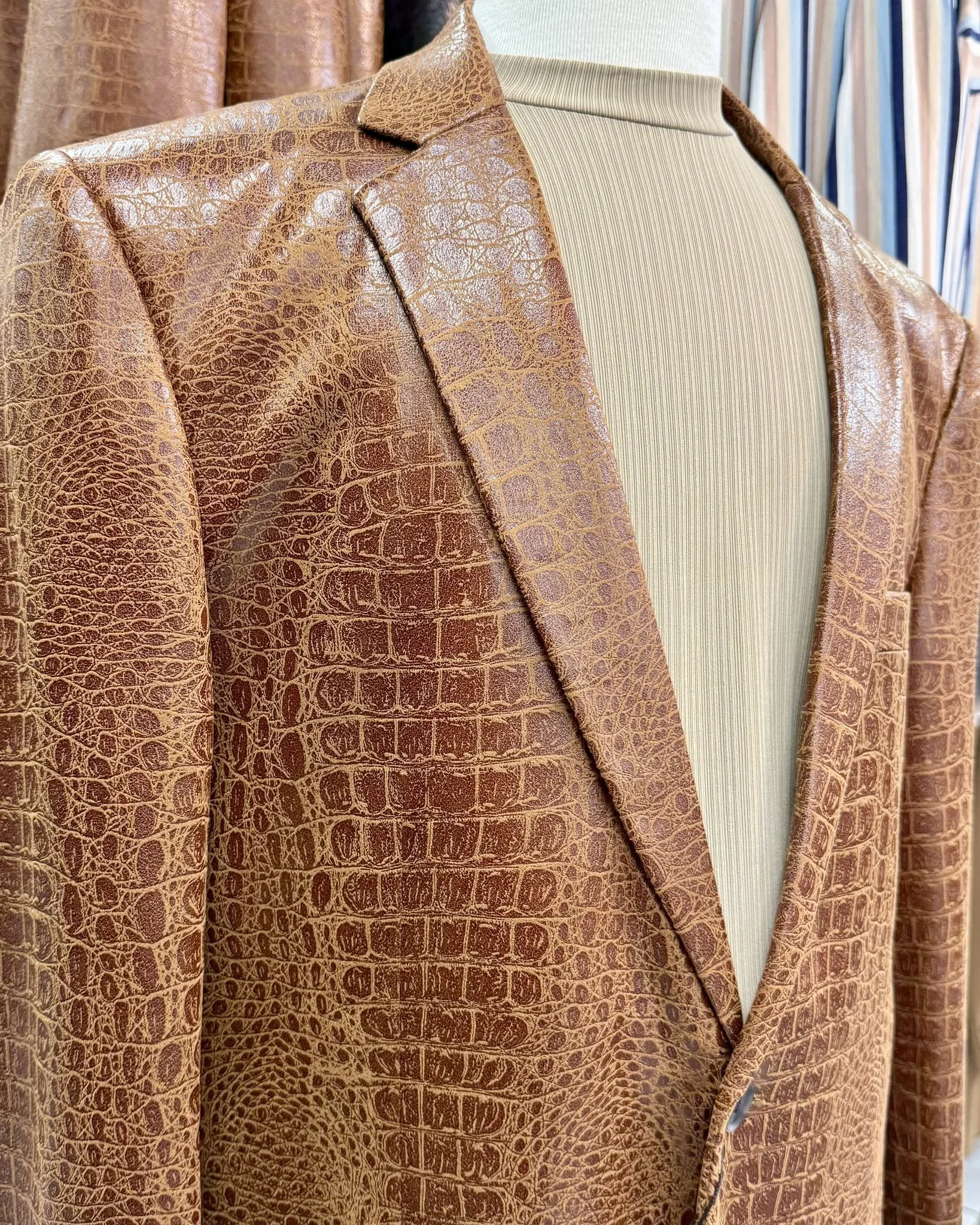Close-up of a brown crocodile-textured leather blazer over a beige ribbed turtleneck sweater