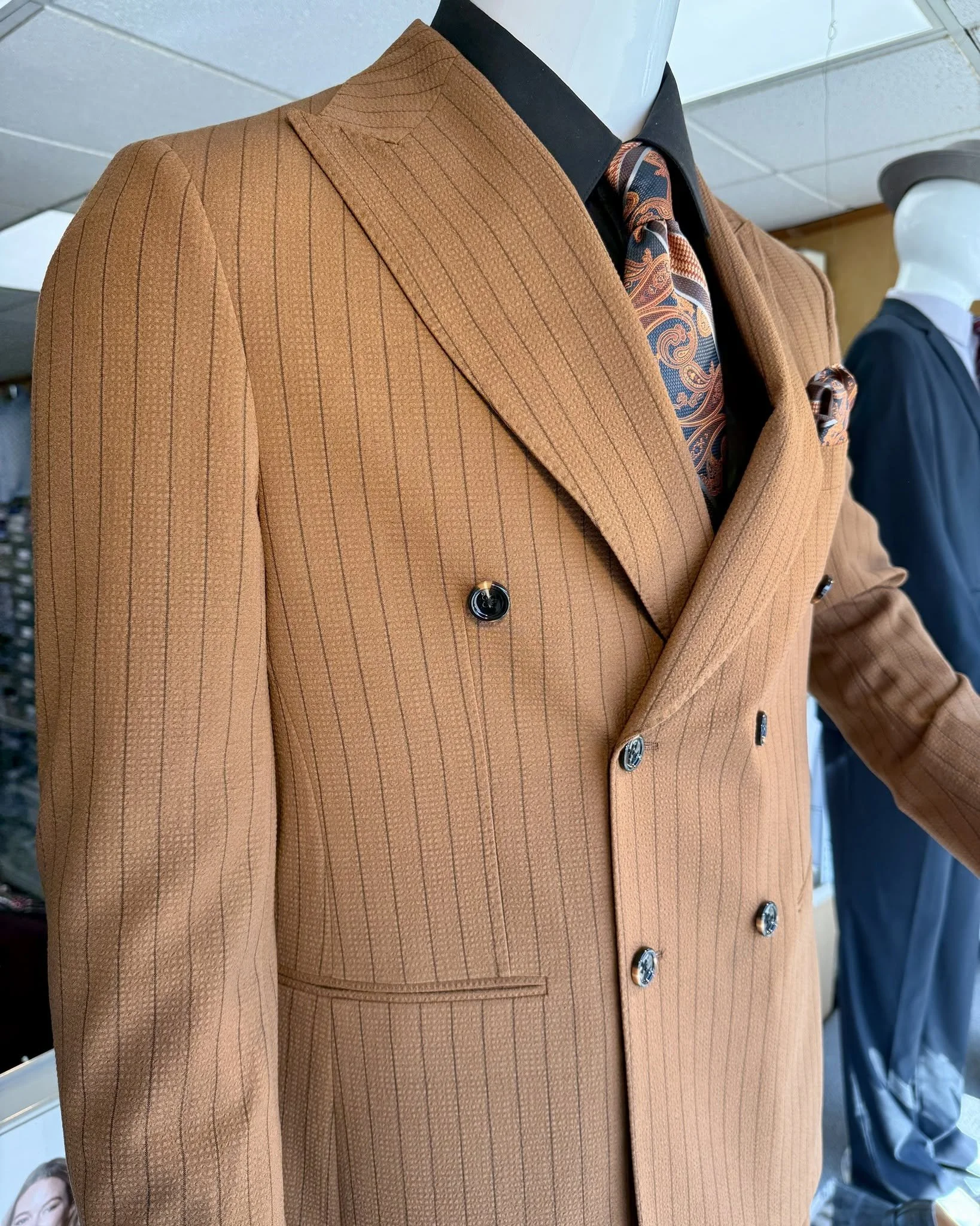 Close-up of a camel-brown pinstripe double-breasted suit with peak lapels, patterned paisley tie, and black pocket square