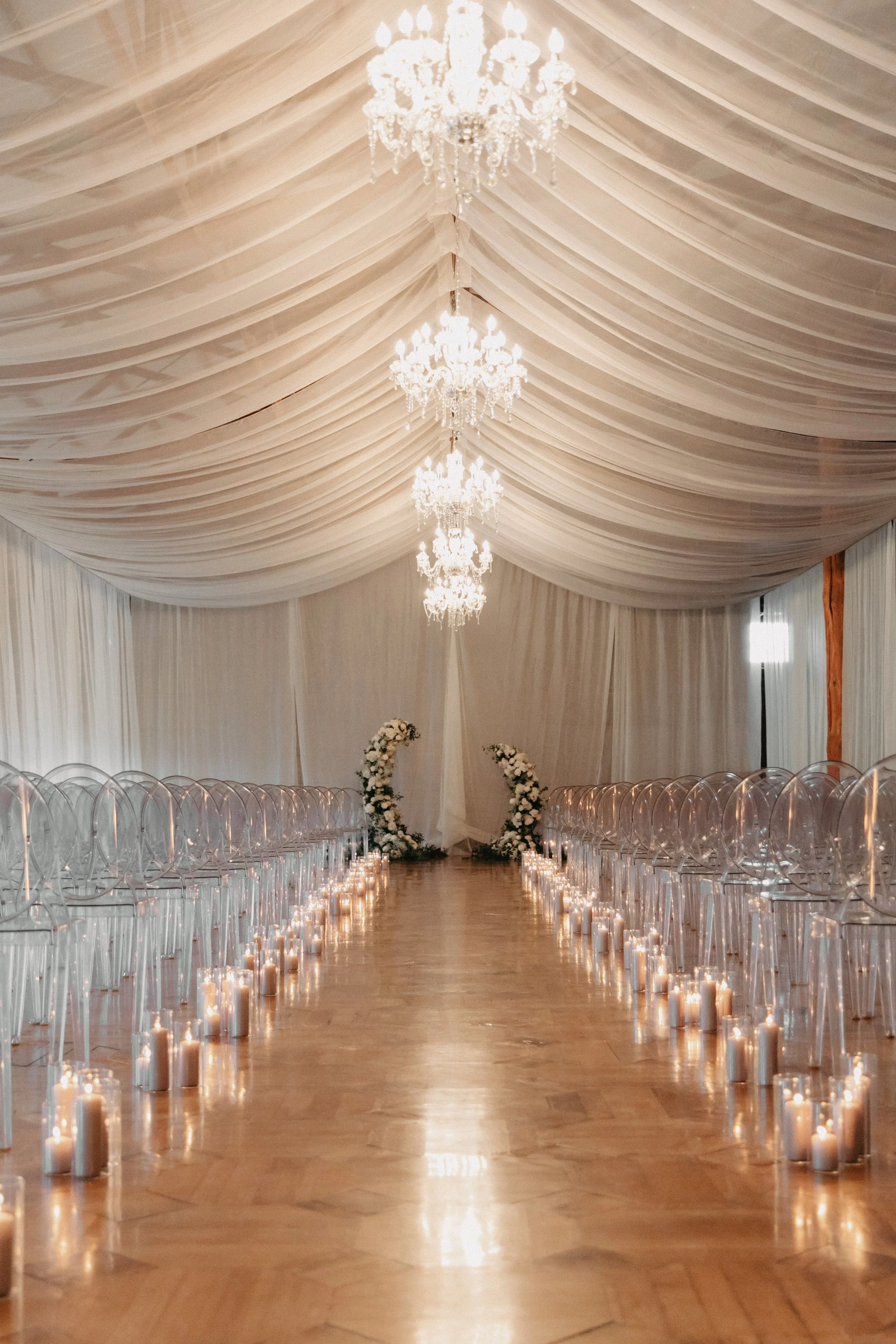white sheer draped ceremony space with a candle lined aisle and ghost chairs for a winter wedding at maysara winery