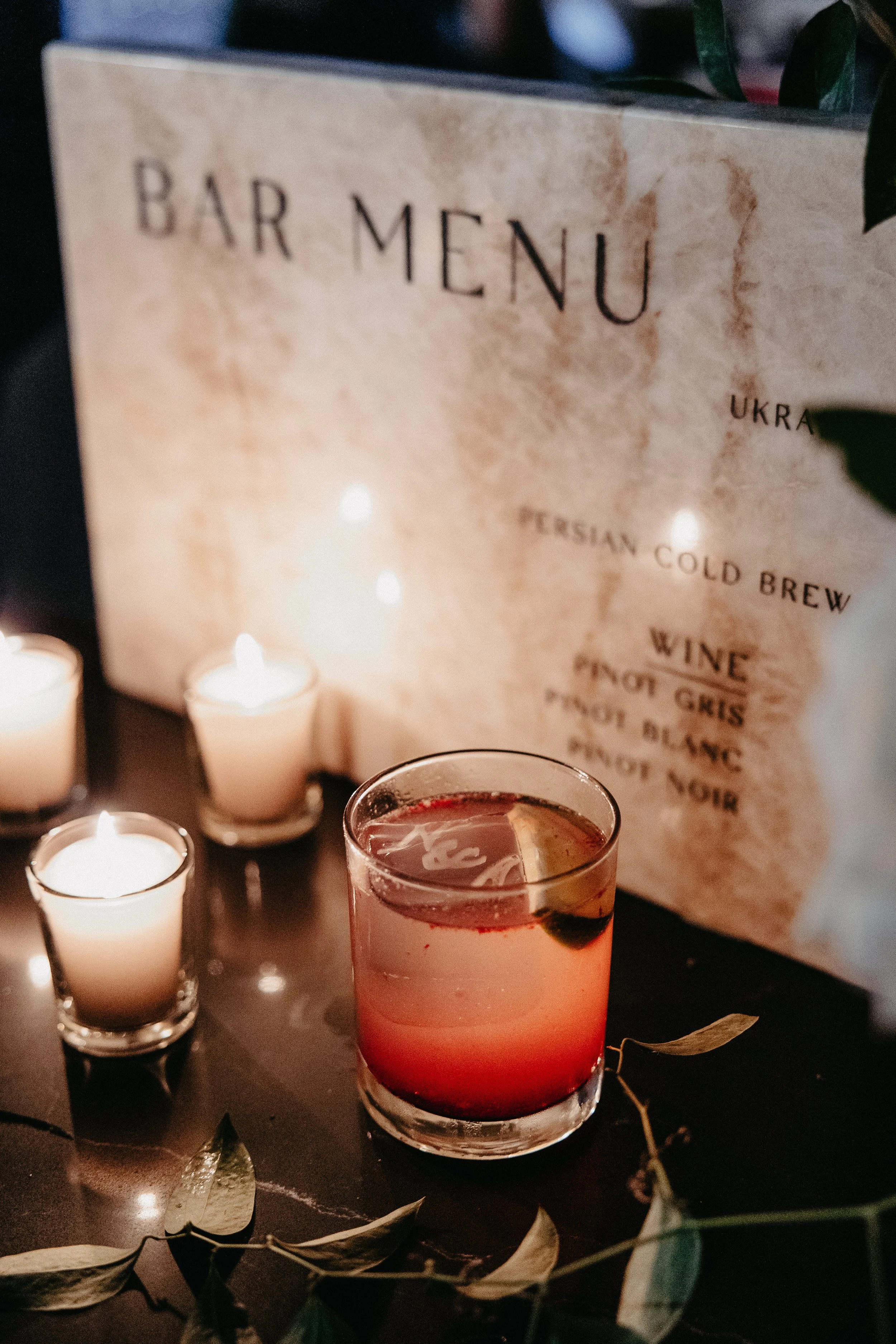 signature cocktail with monogram ice cube in front of custom stone bar menu at winter wedding at maysara winery