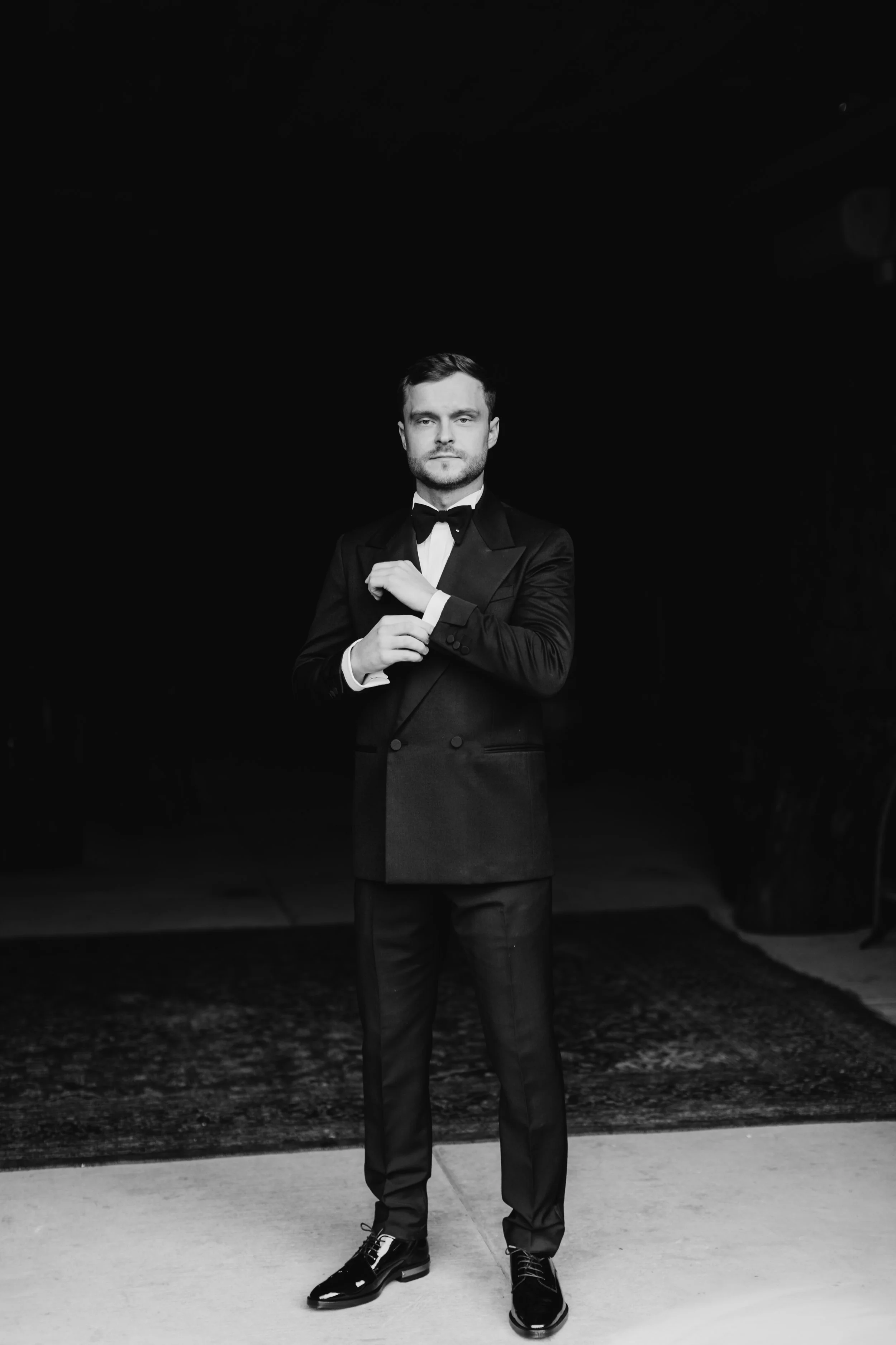 Black and white portrait of groom adjusting cufflinks in Gucci tuxedo before winter wedding at Maysara Winery