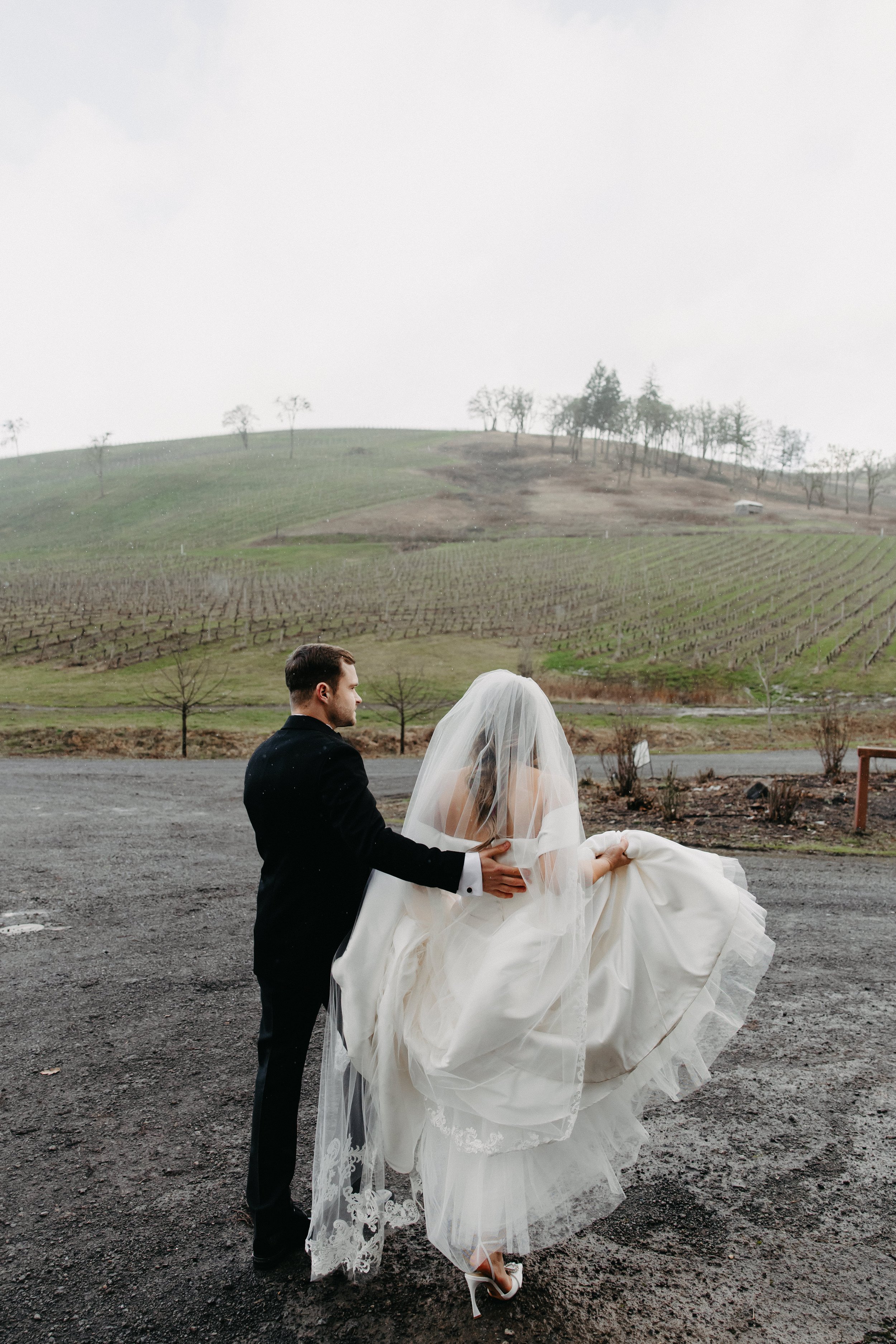 Bride and groom walking in front of vineyard during the rain