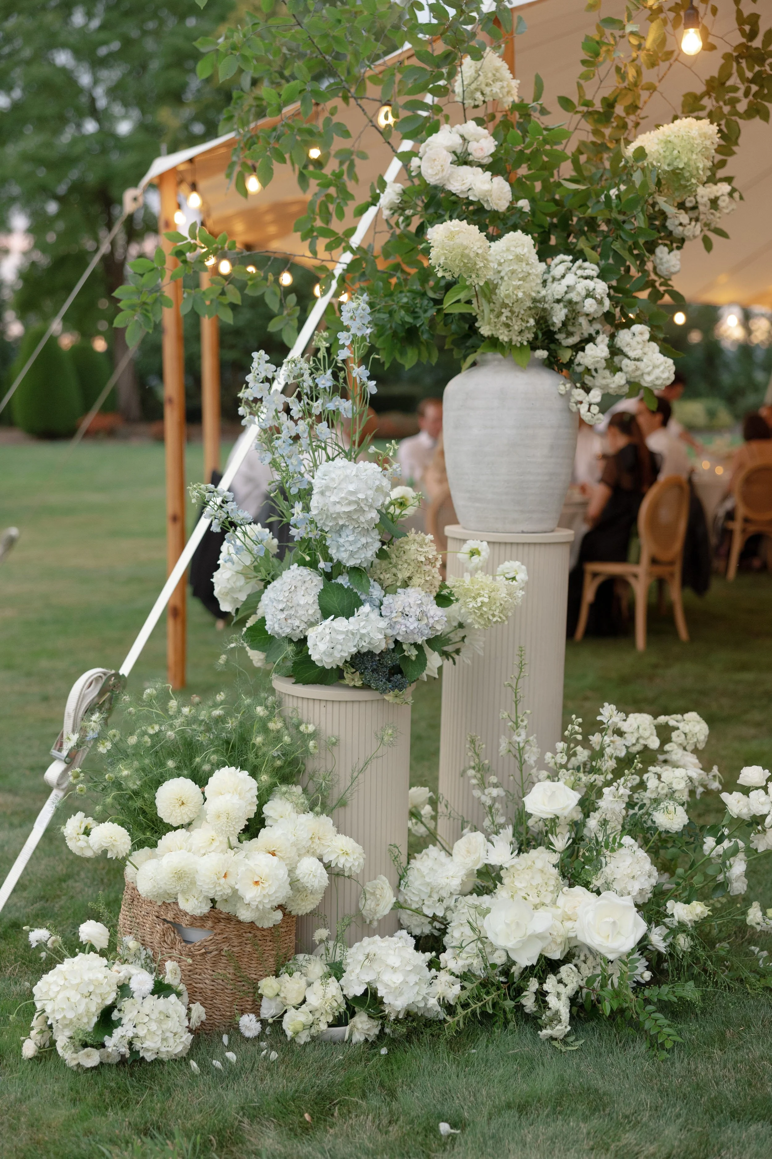 lush green and white florals on wood risers framing wedding reception tent