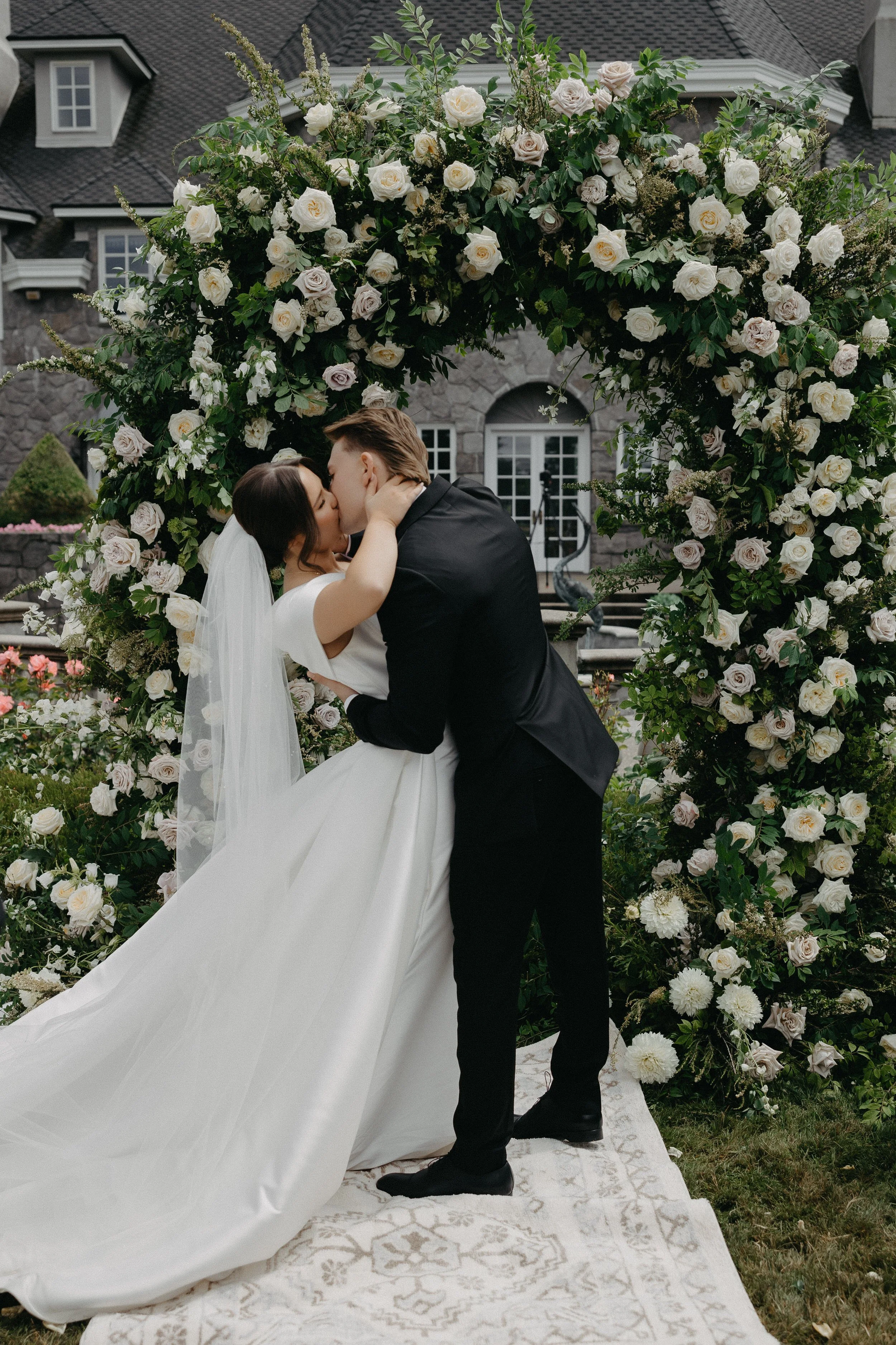 Bride and groom kiss under grand wedding ceremony floral arch