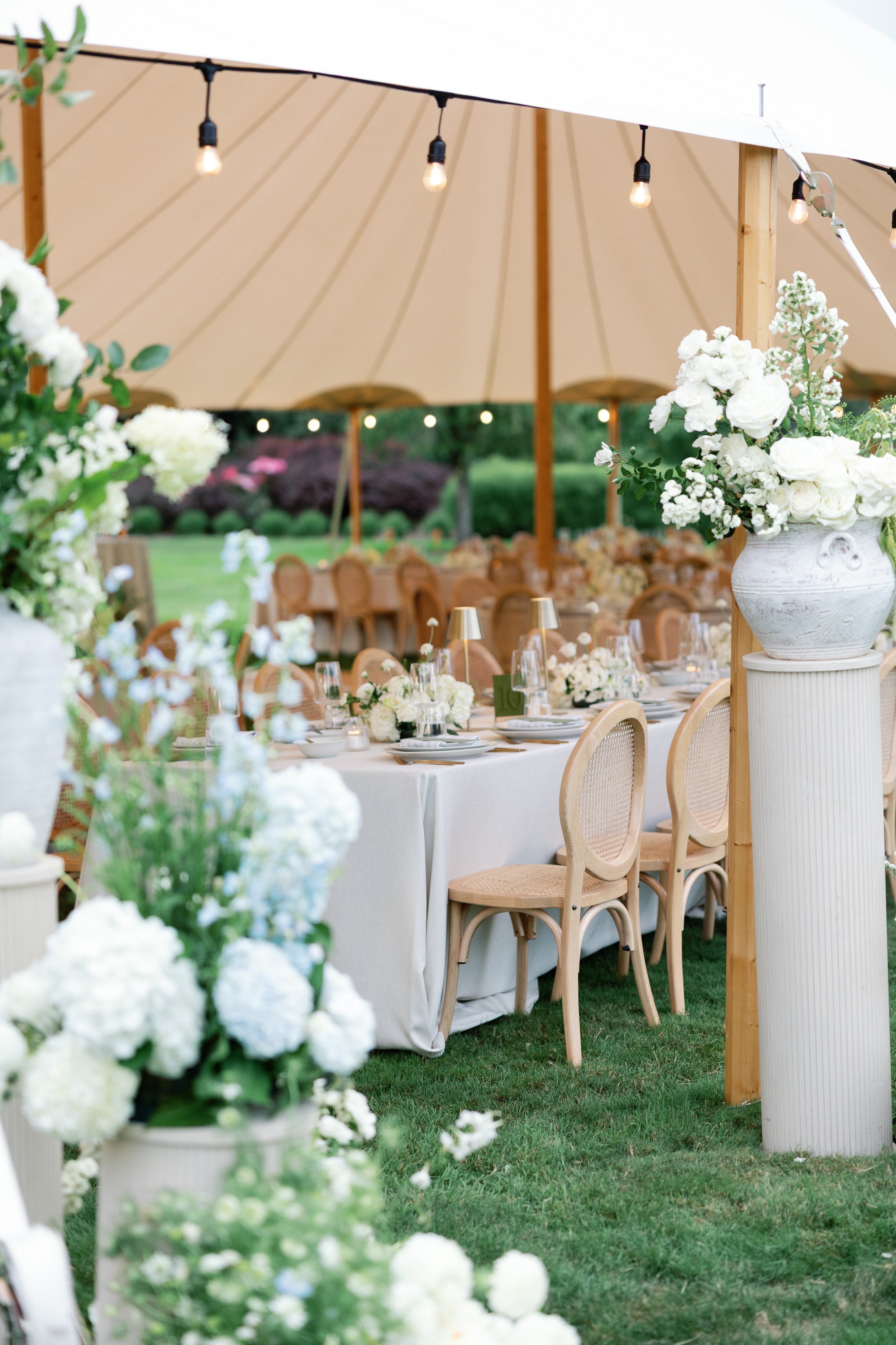 Wedding reception tent with lush green and white florals framing entrance to tent and tables in background