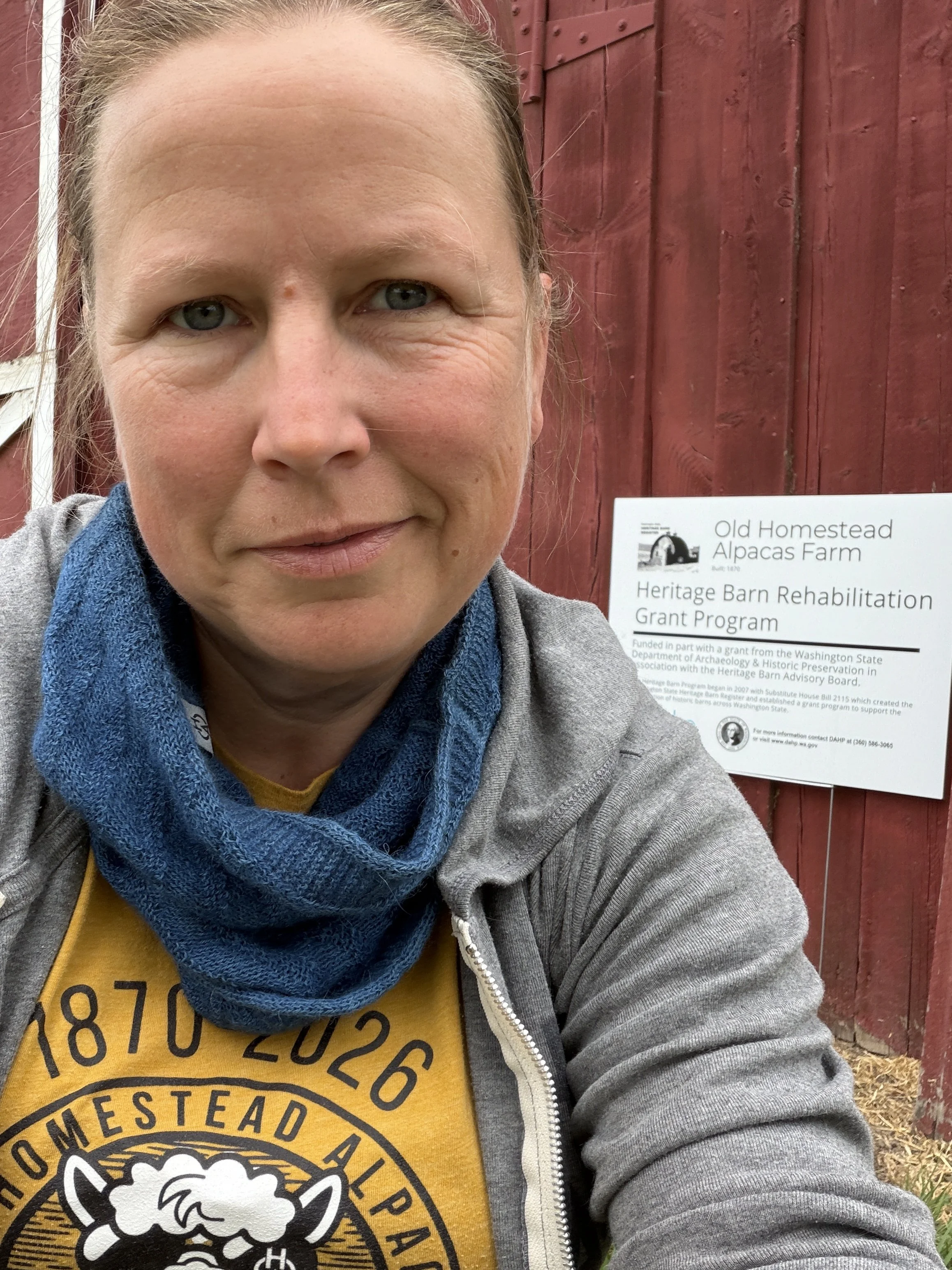 A woman taking a selfie in front of a sign at Old Homestead Alpacas Farm. The sign reads: Heritage Barn Rehabilitation Grant Program.
