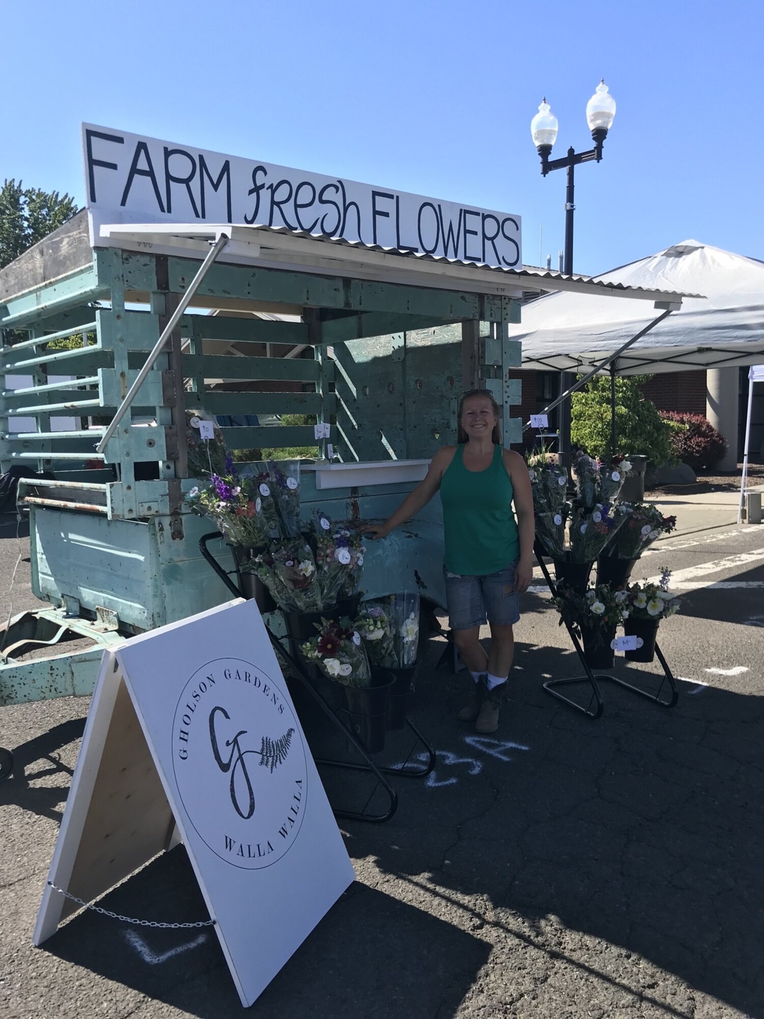 a woman standing beside a roadside farm stand selling fresh cut flowers