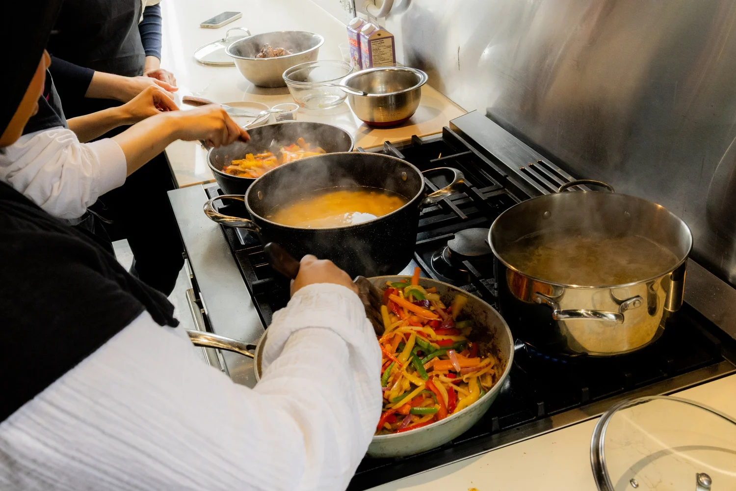 Hands stirring colourful peppers in a pan on a busy workshop stove