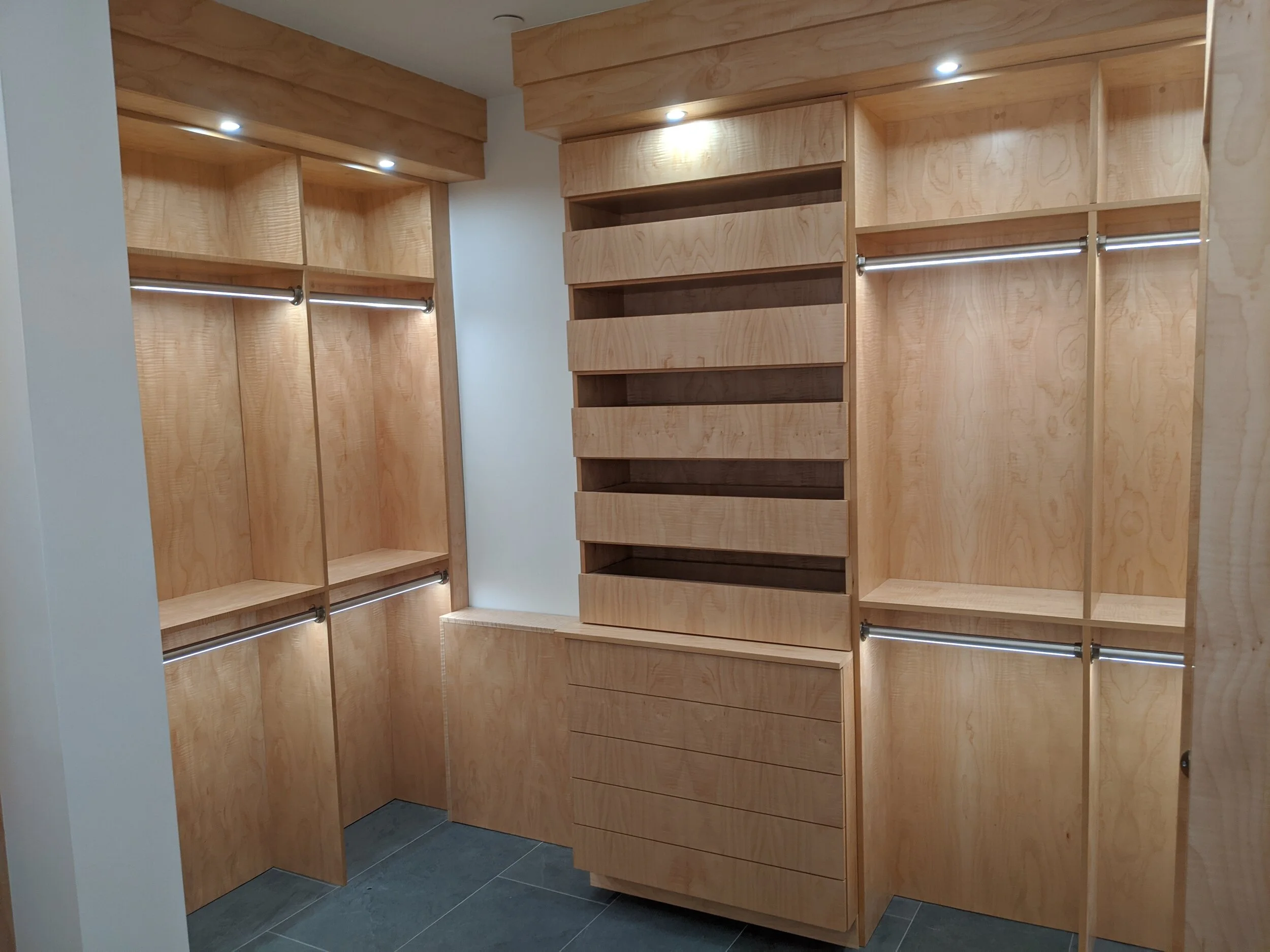 A custom-built walk-in closet with wooden cabinetry, open shelving, and hanging rods, illuminated by ceiling spotlights.