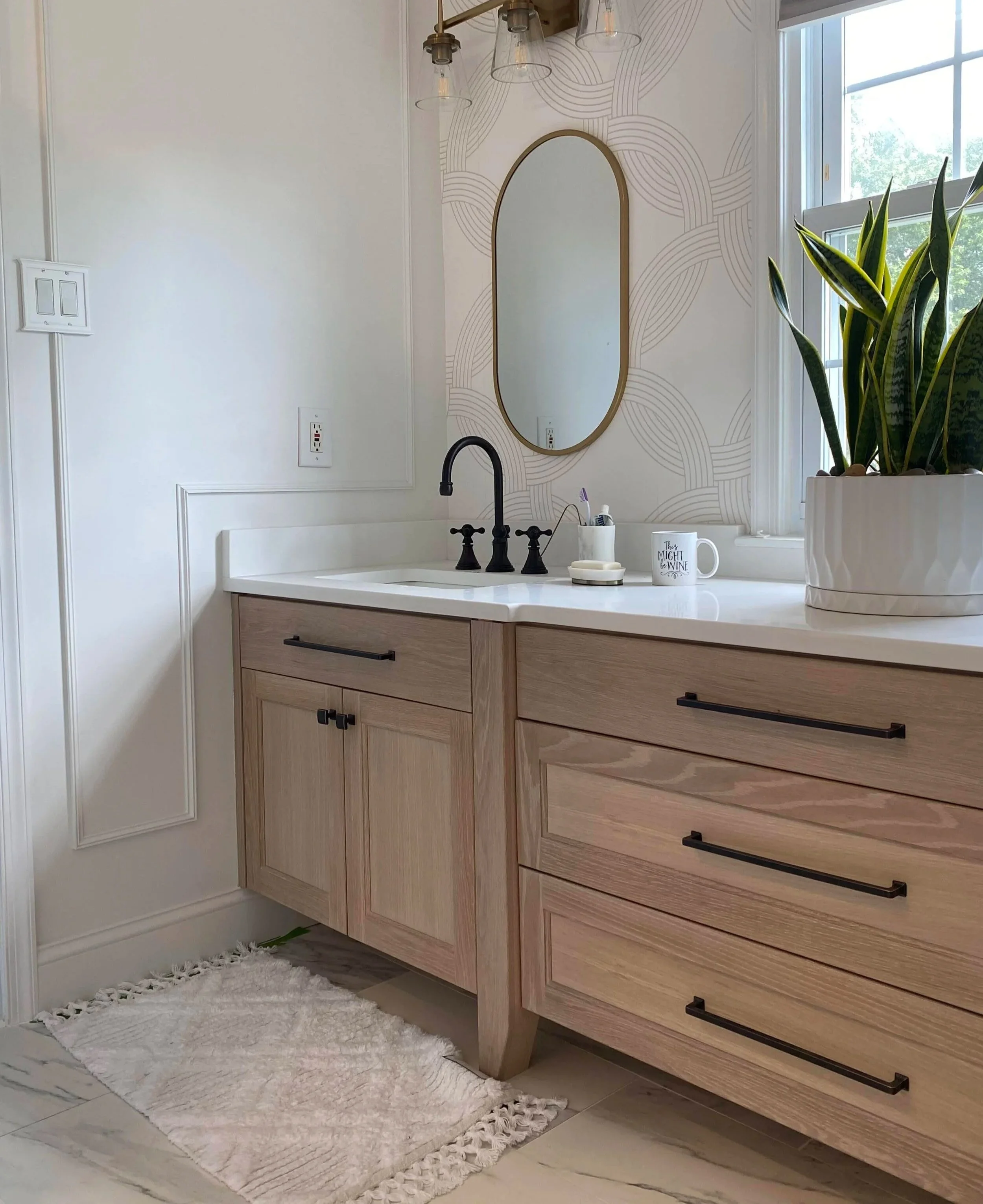 A bathroom vanity with a white countertop, black faucet, and a large potted plant near a window.