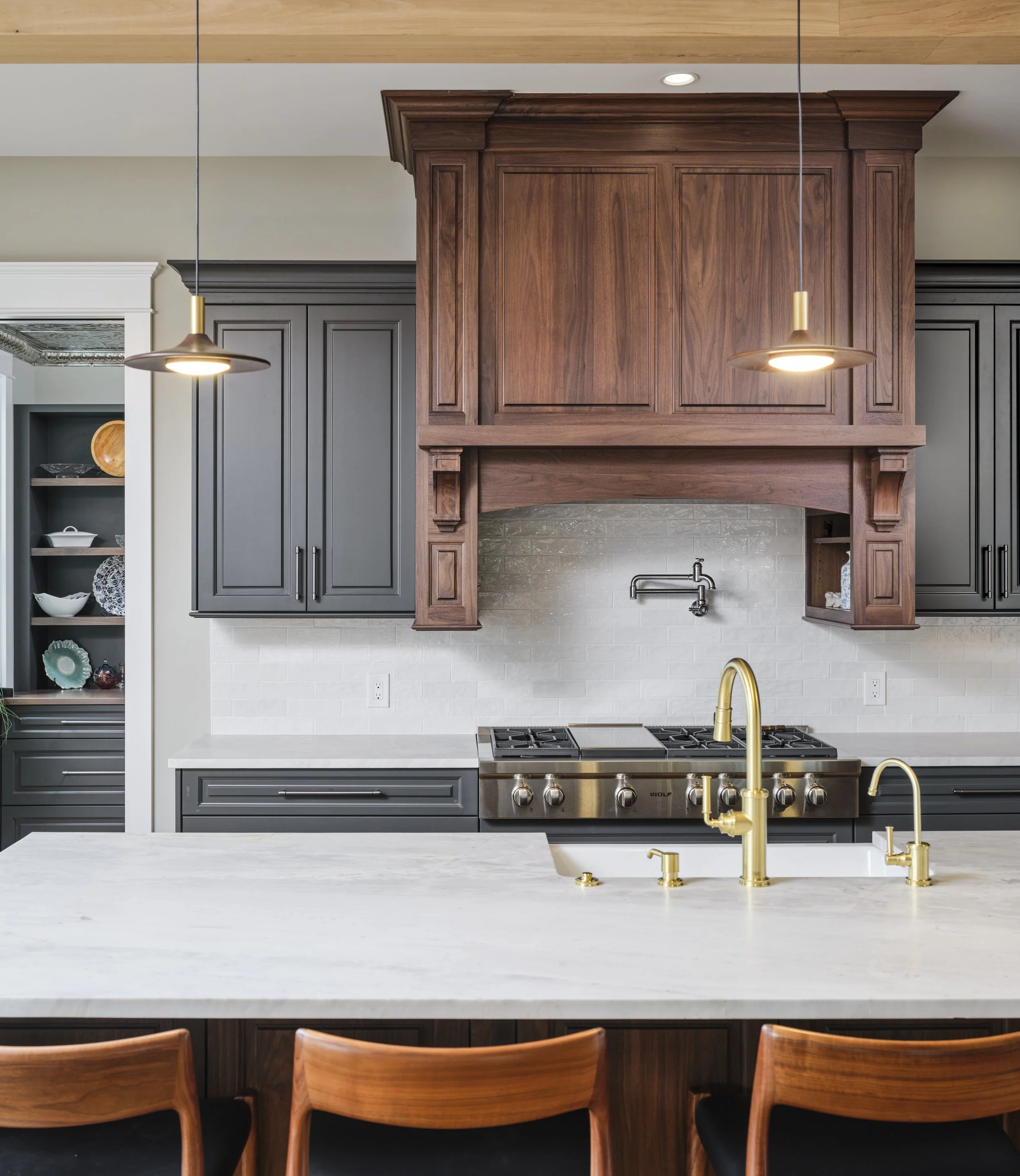 Modern kitchen with dark gray cabinets, a white subway tile backsplash, and a large white marble island with gold fixtures.