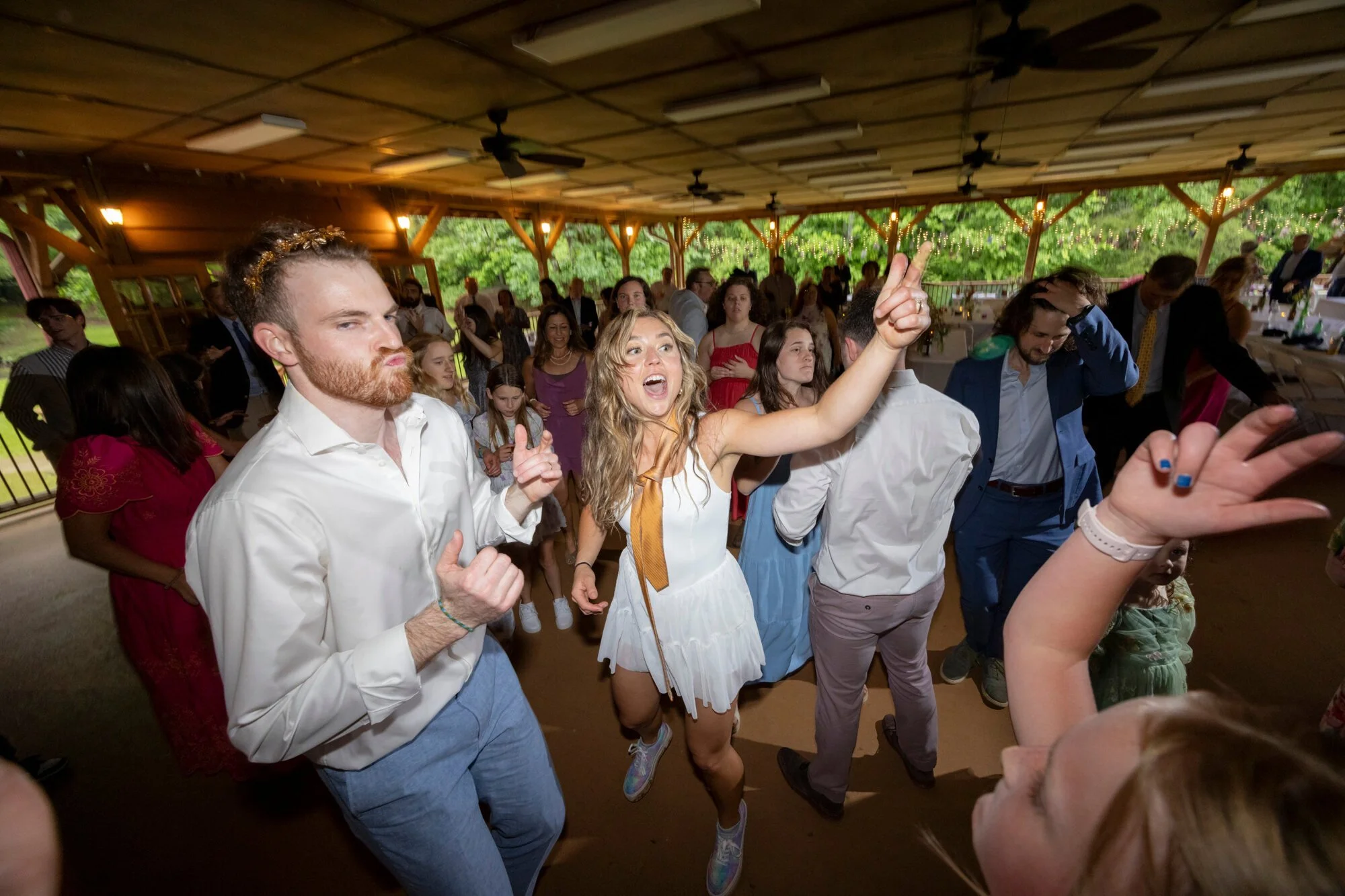 People dancing and celebrating at an indoor event with string lights and wooden decor.
