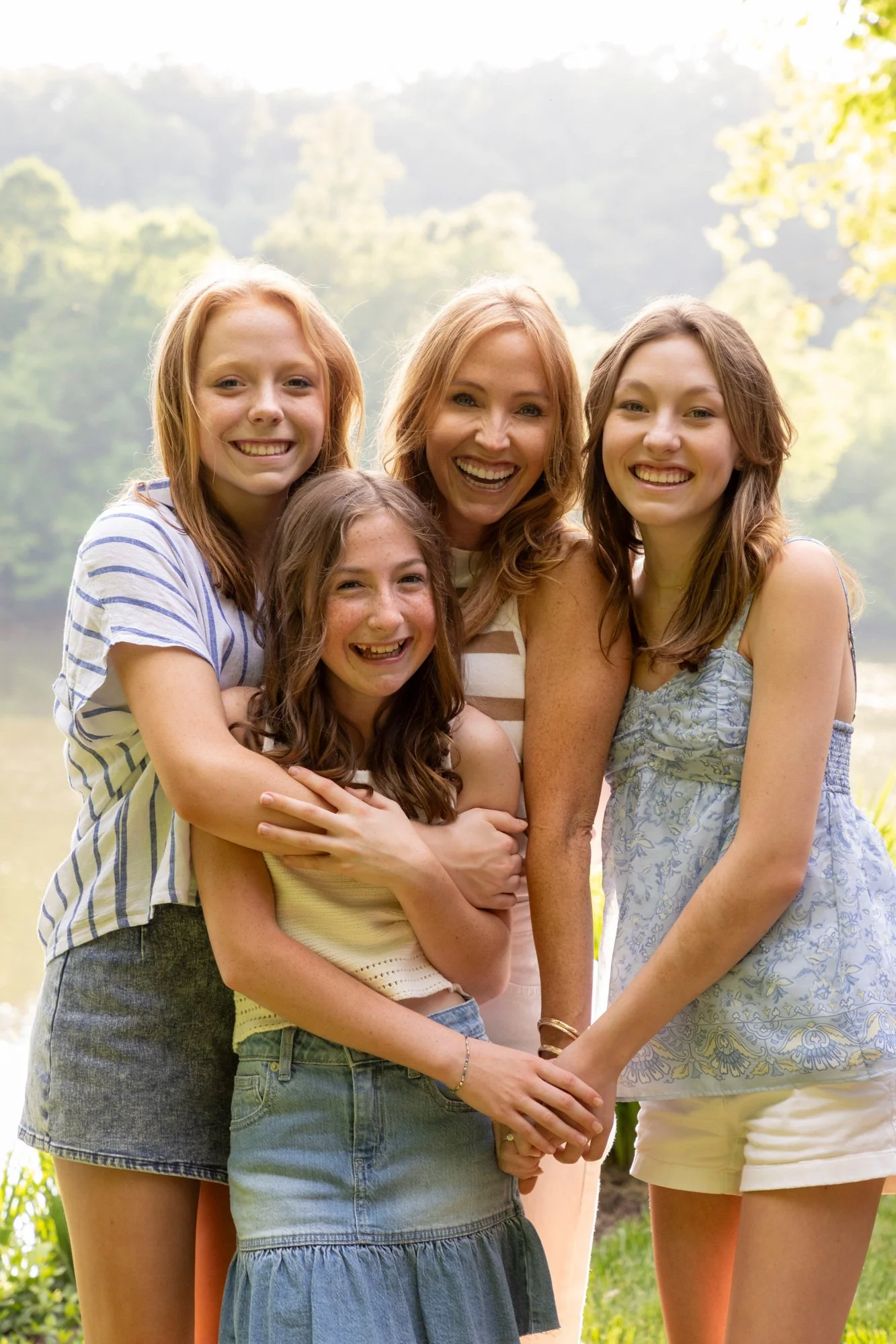 Group of five people, three women and two girls, smiling outdoors in a park on a sunny day.