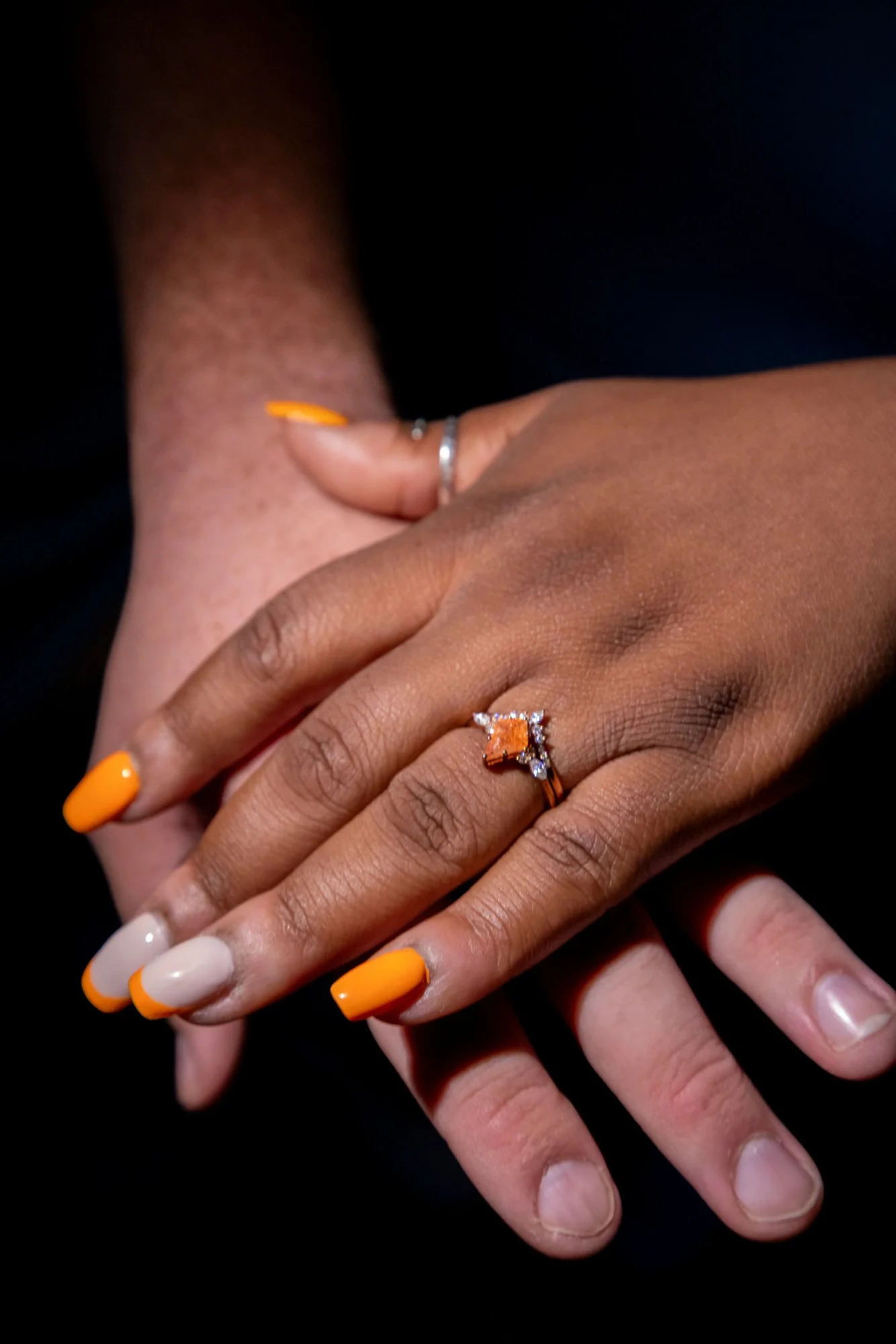 Close-up of pairs of hands with painted nails and a ring on one finger, against a black background.