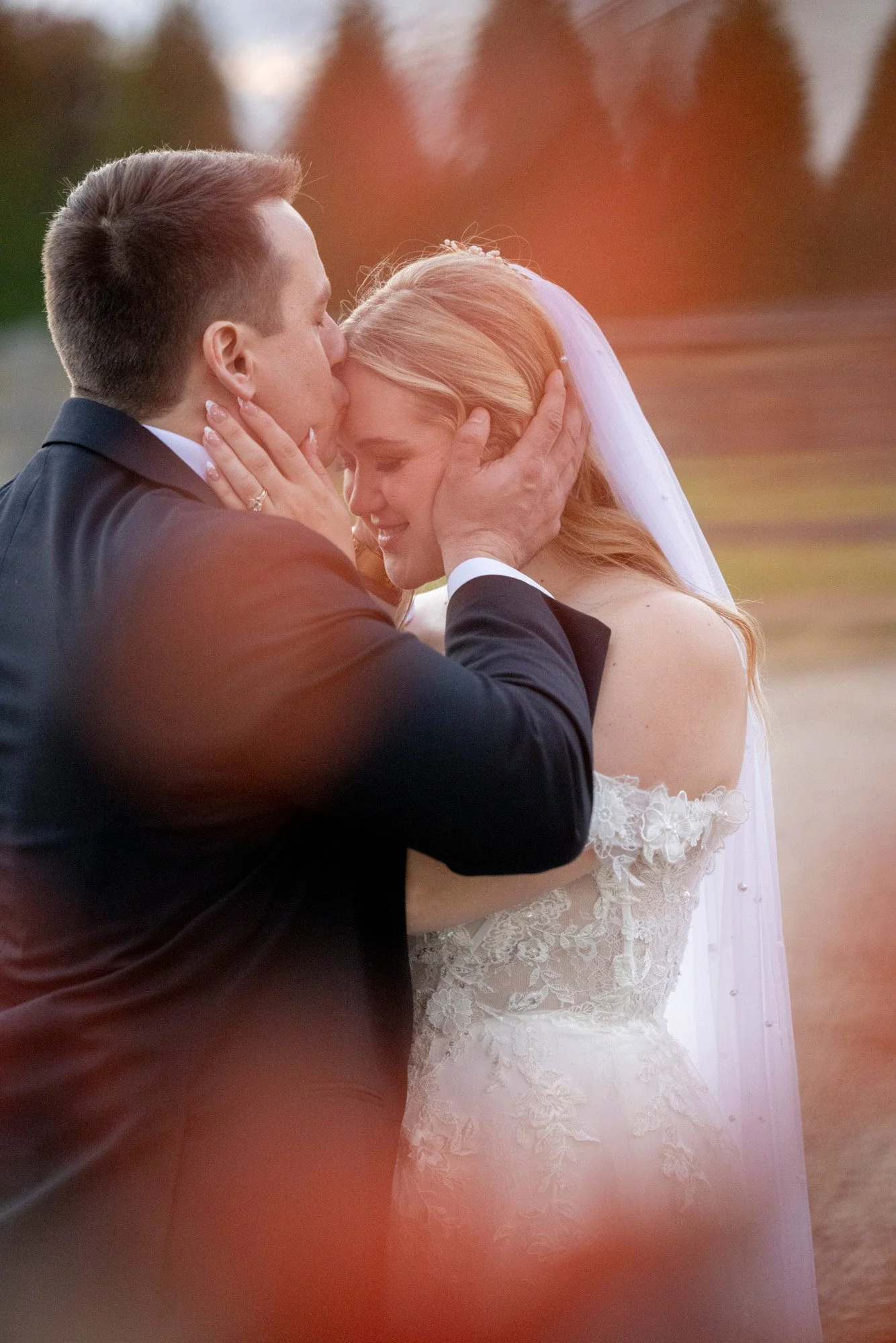 A bride and groom sharing a kiss during their wedding ceremony, with a blurred outdoor background.