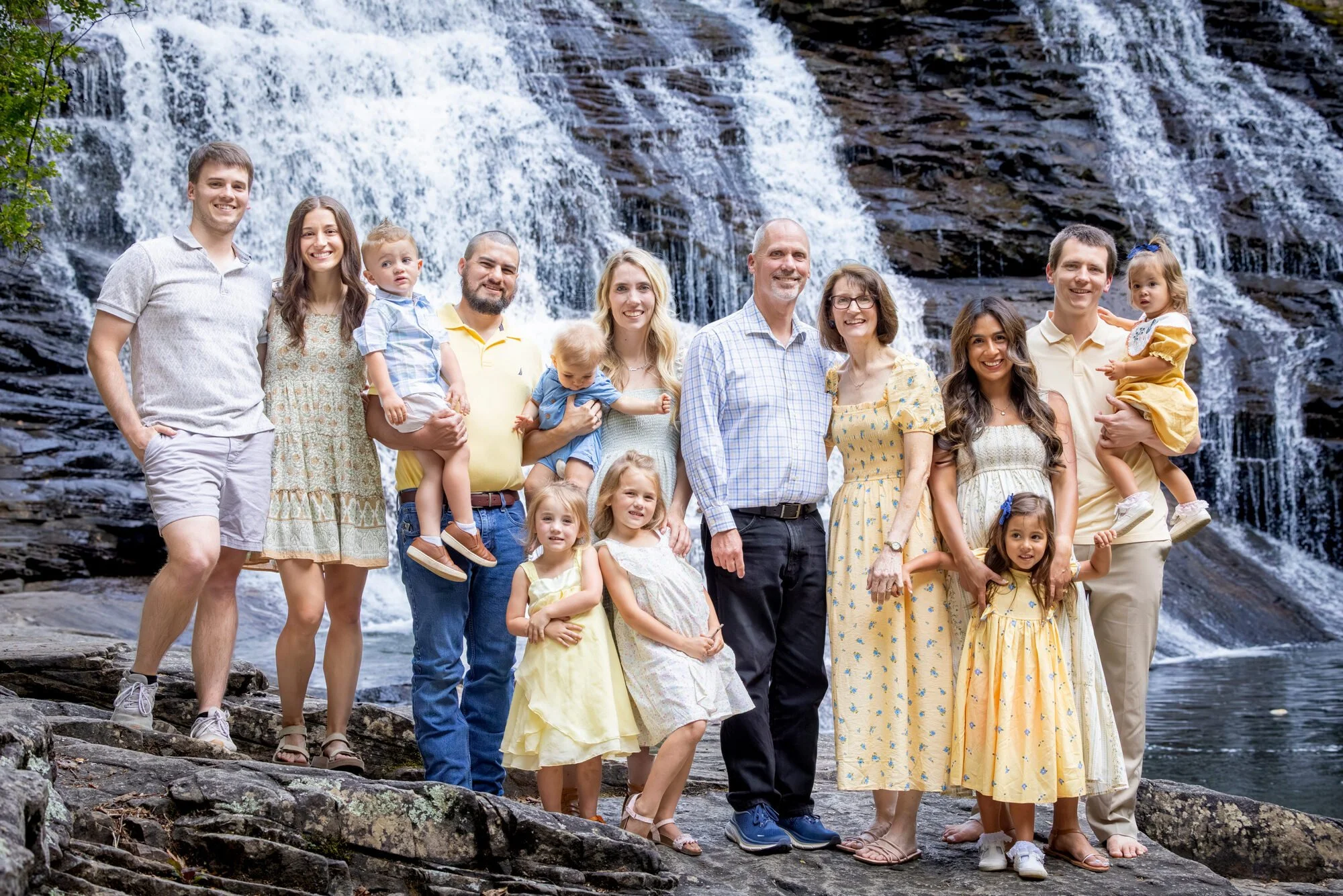 A family of adults and children posing together outdoors near a waterfall.
