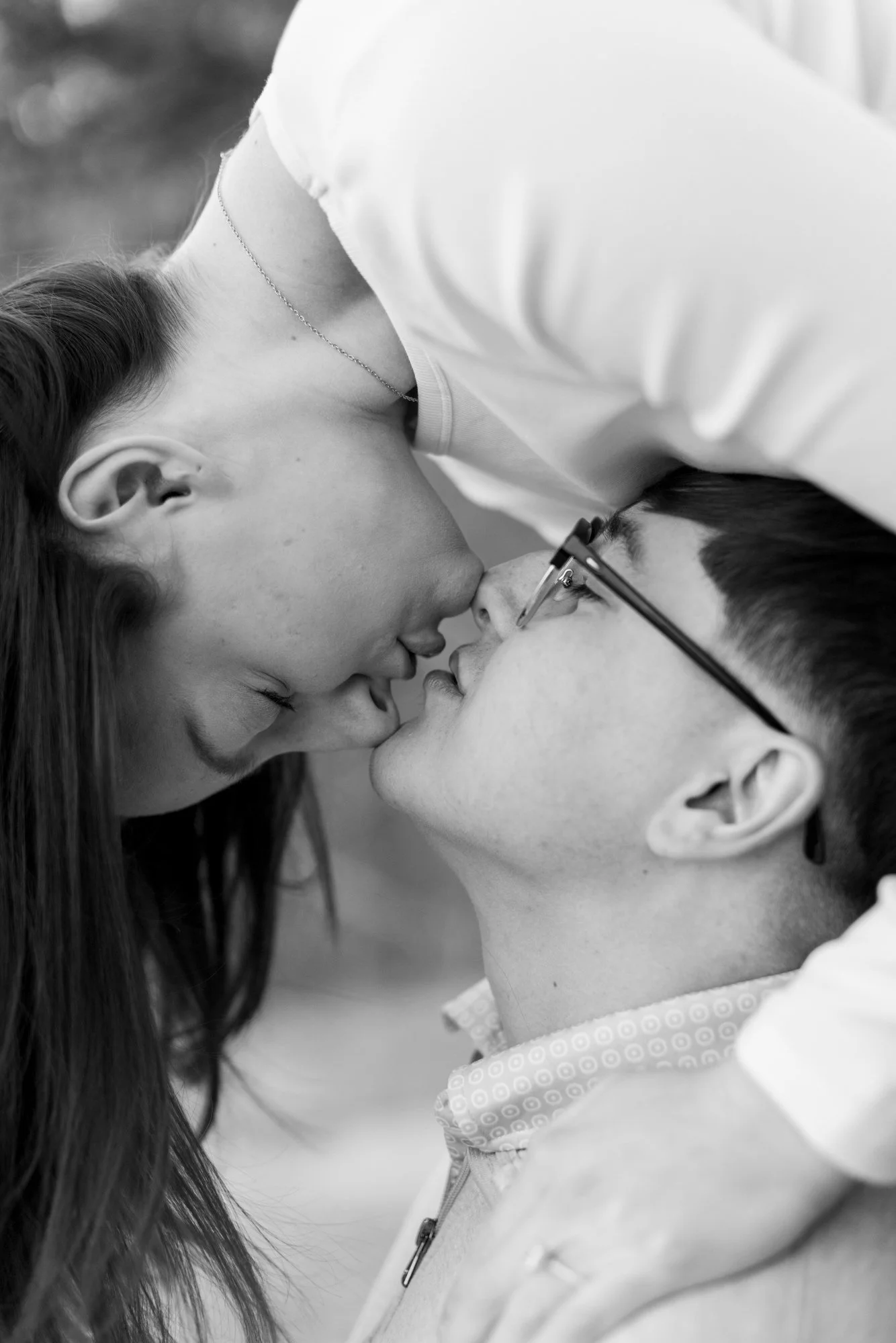 A black-and-white photo of a couple with their foreheads touching, eyes closed, in an intimate moment. The woman has long hair and is wearing a necklace, while the man has short hair and glasses.