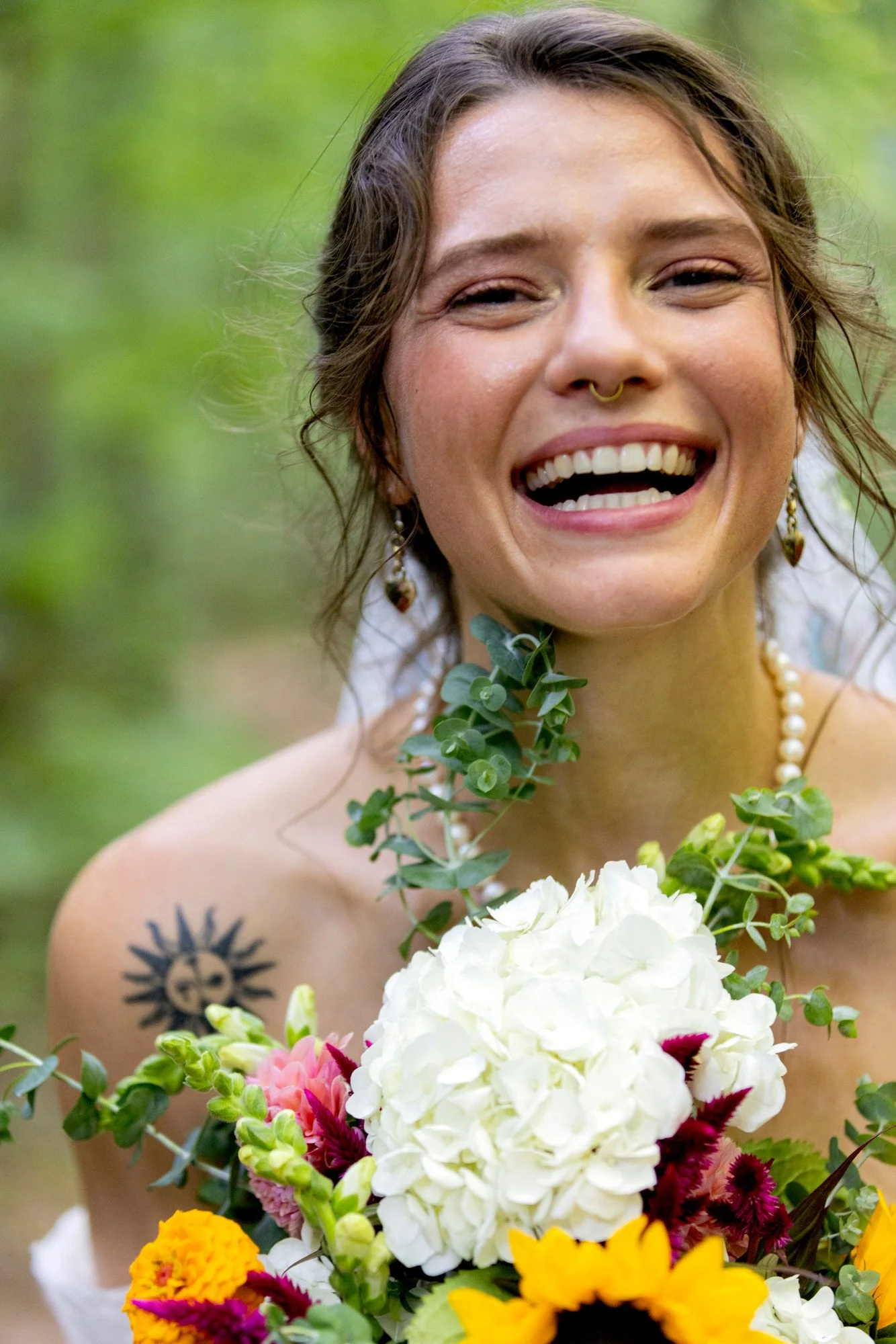 A woman with a wide smile holding a bouquet of various colorful flowers, with a green blurred background.