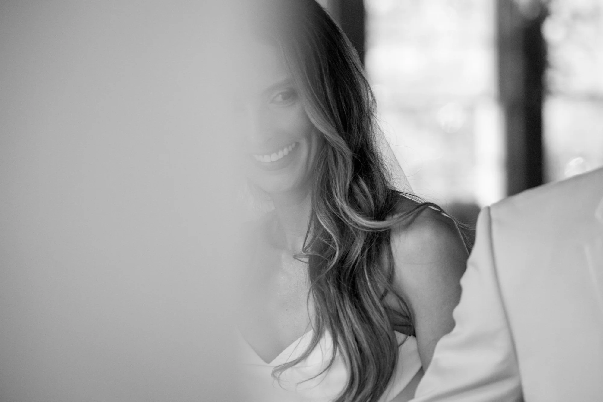 A woman with long, wavy hair smiling, partially obscured by a semi-transparent surface, in black and white.