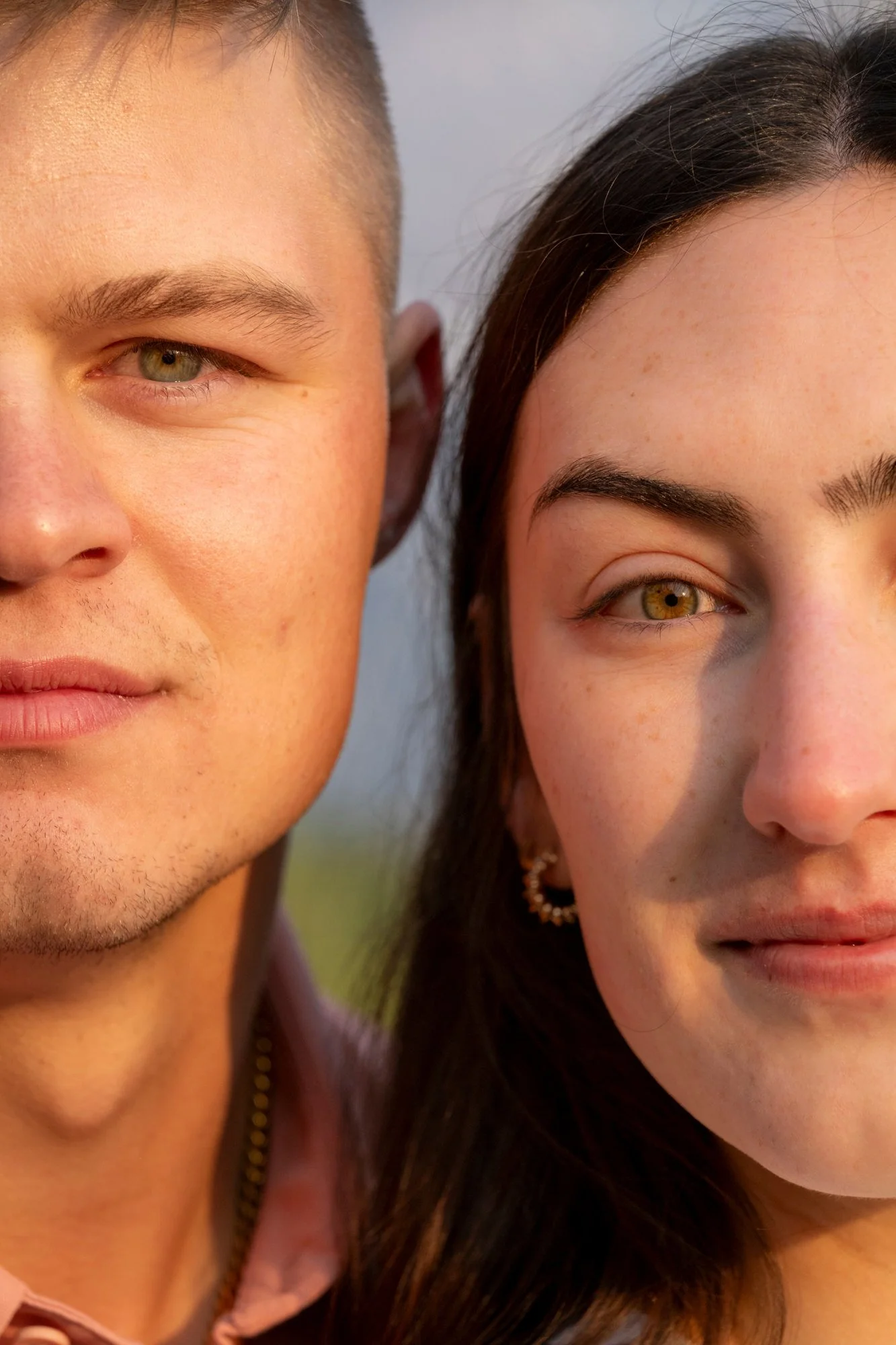 Close-up of a young man and woman standing closely together, winking at the camera, with a blurred outdoor background.