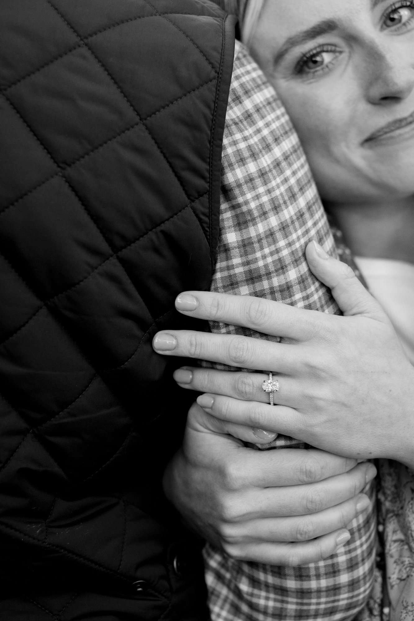 A woman wearing a ring on her finger is hugging a person dressed in a checked shirt, with their face partially visible from the nose down.