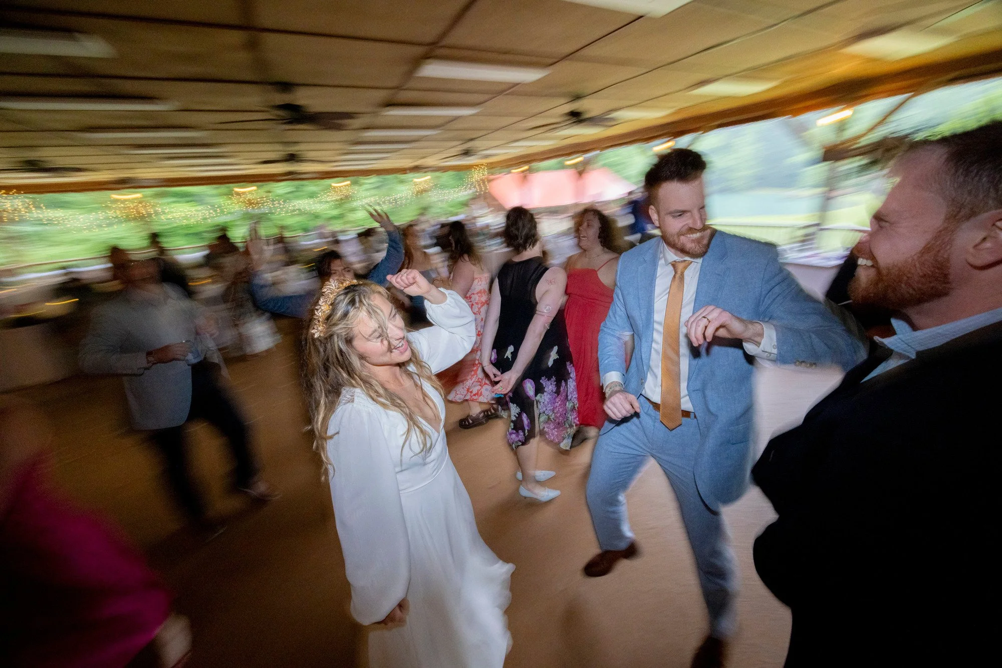 People dancing and enjoying themselves at a party or celebration, with some smiling and others moving to the music, under a decorated ceiling with string lights.