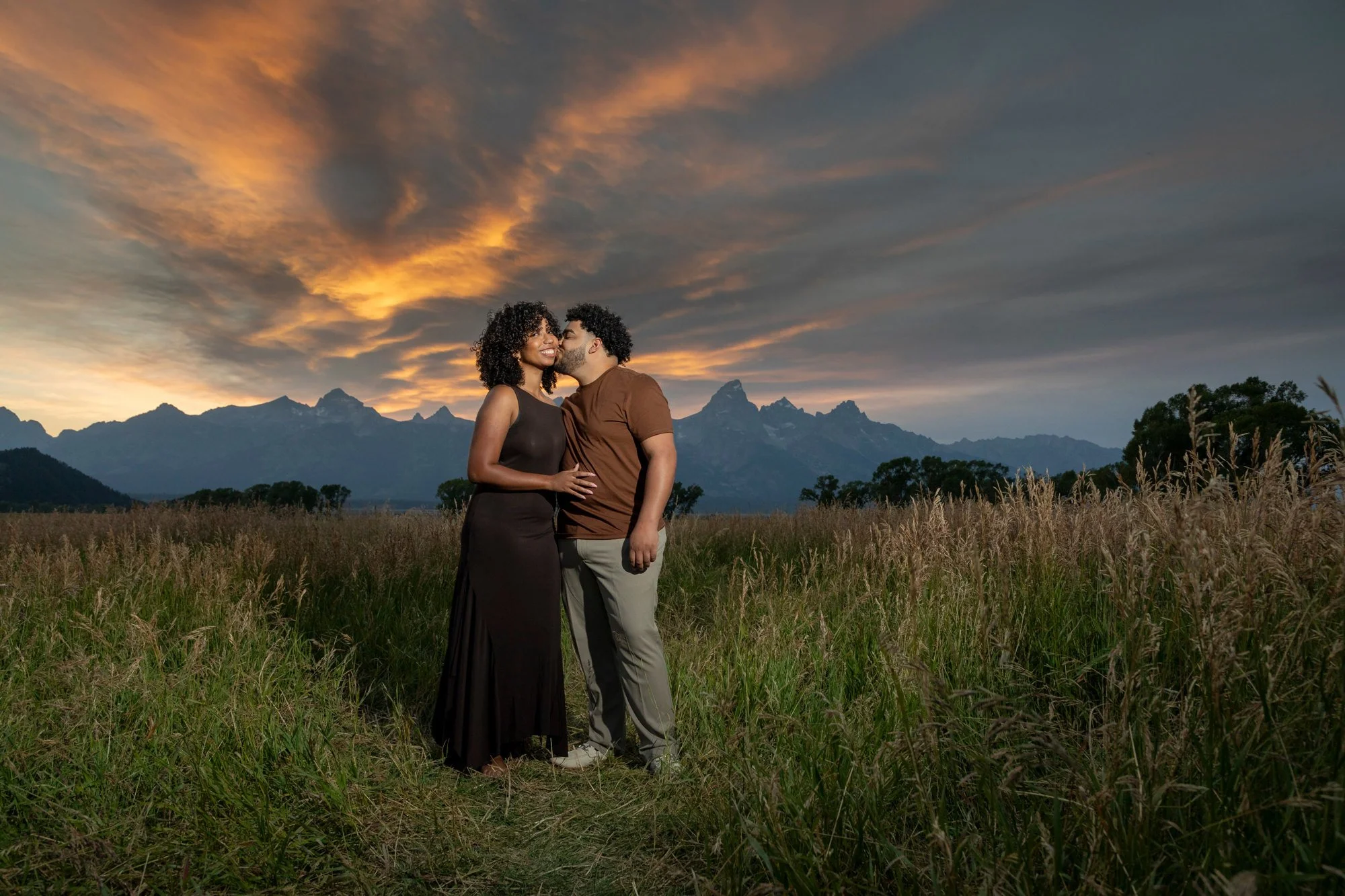 A couple standing in a field at sunset with mountains in the background, sharing an intimate moment.