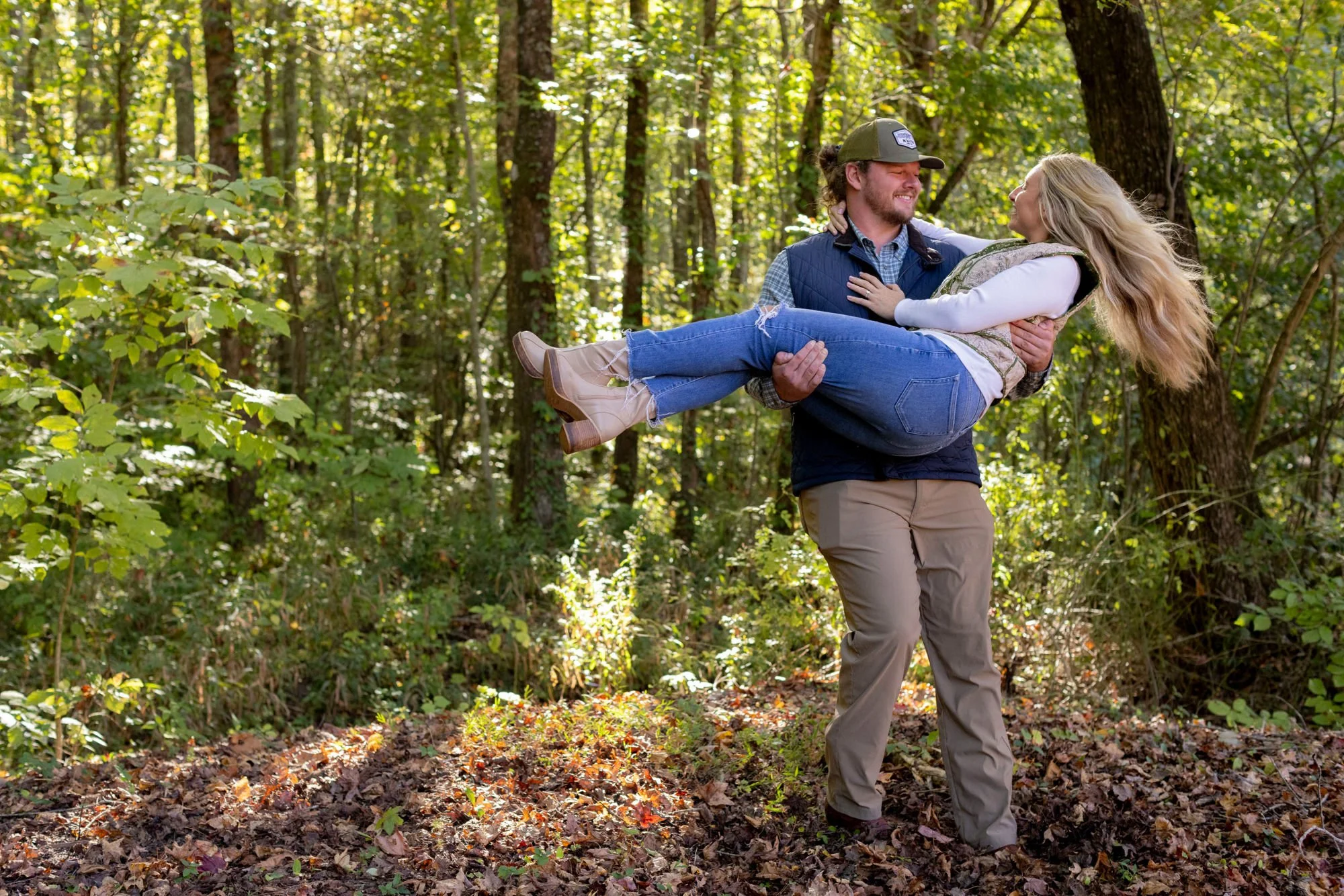 A man carrying a woman in his arms in a forested area during daytime.