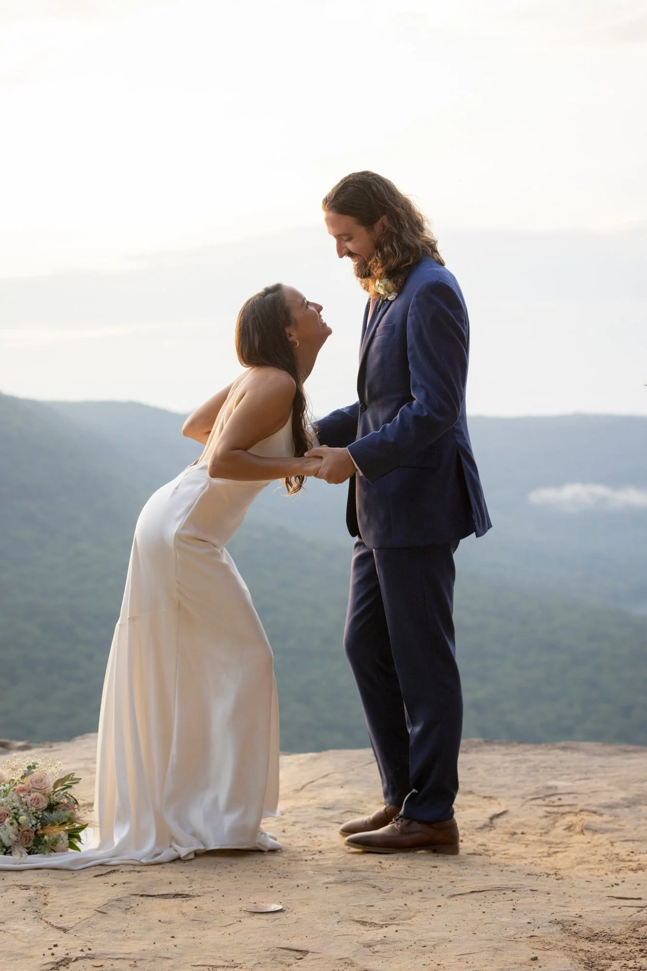 A couple getting married outdoors on a mountain, holding hands and looking at each other lovingly.