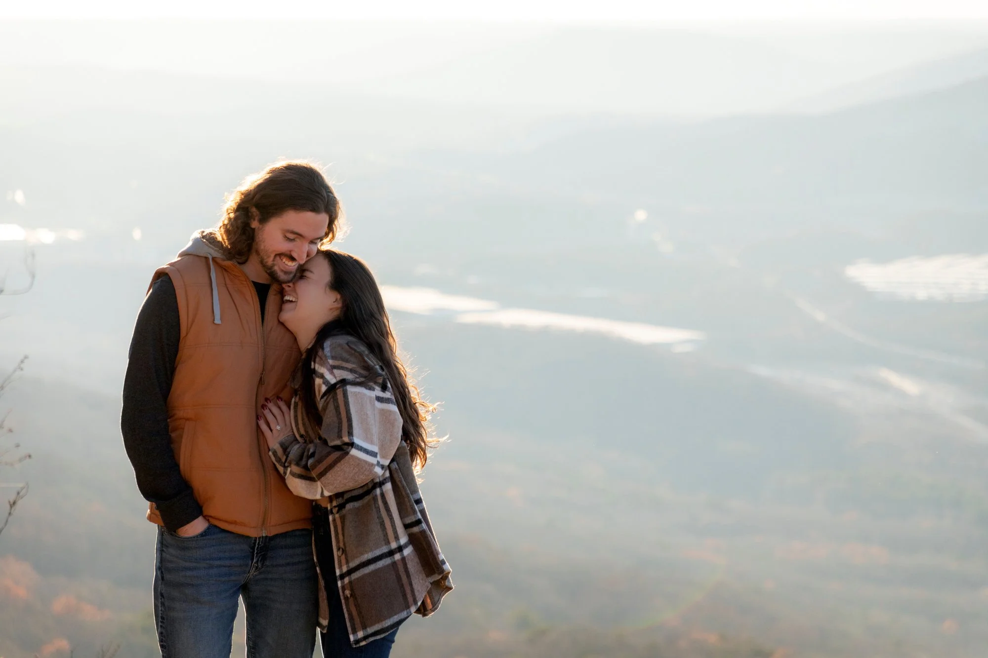 A couple sharing a joyful embrace outdoors near a body of water during sunset or sunrise.