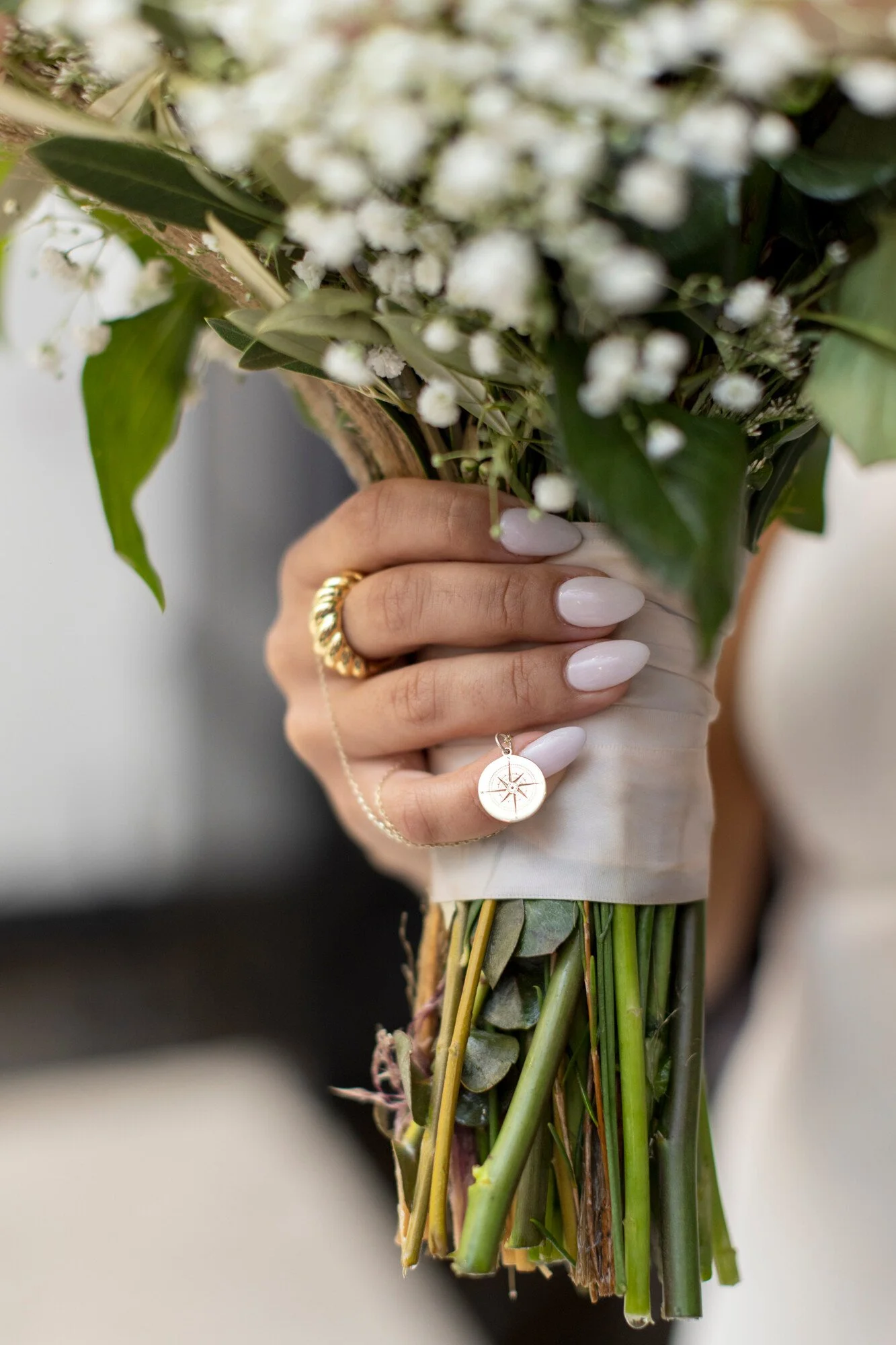 Close-up of a person's hand holding a bouquet of white flowers and green leaves, with part of the stems visible.